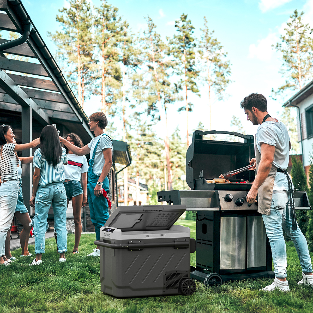 Mensen barbecueën in een achtertuin. Een man grilt eten naast een draagbare koelbox.