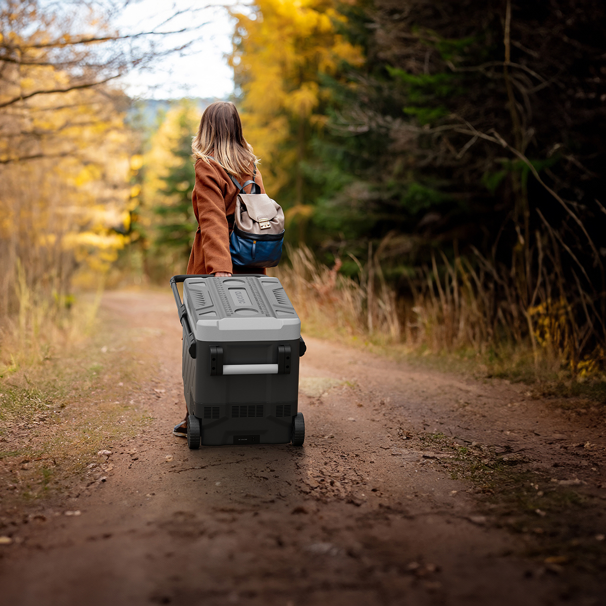 Vrouw met rugzak trekt koelbox over bospad in herfst.