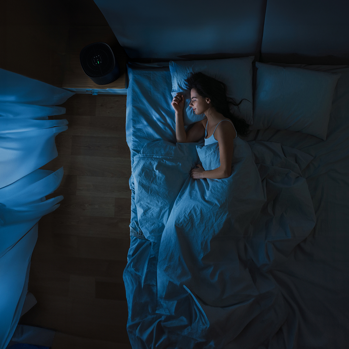 A woman sleeps peacefully in a dark room, with an air purifier on a nightstand.