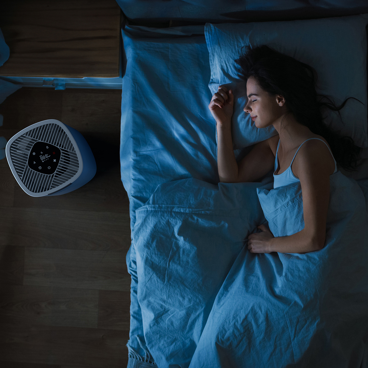 Eine Frau schläft in einem blauen Bett neben einem Luftreiniger auf Holzboden.