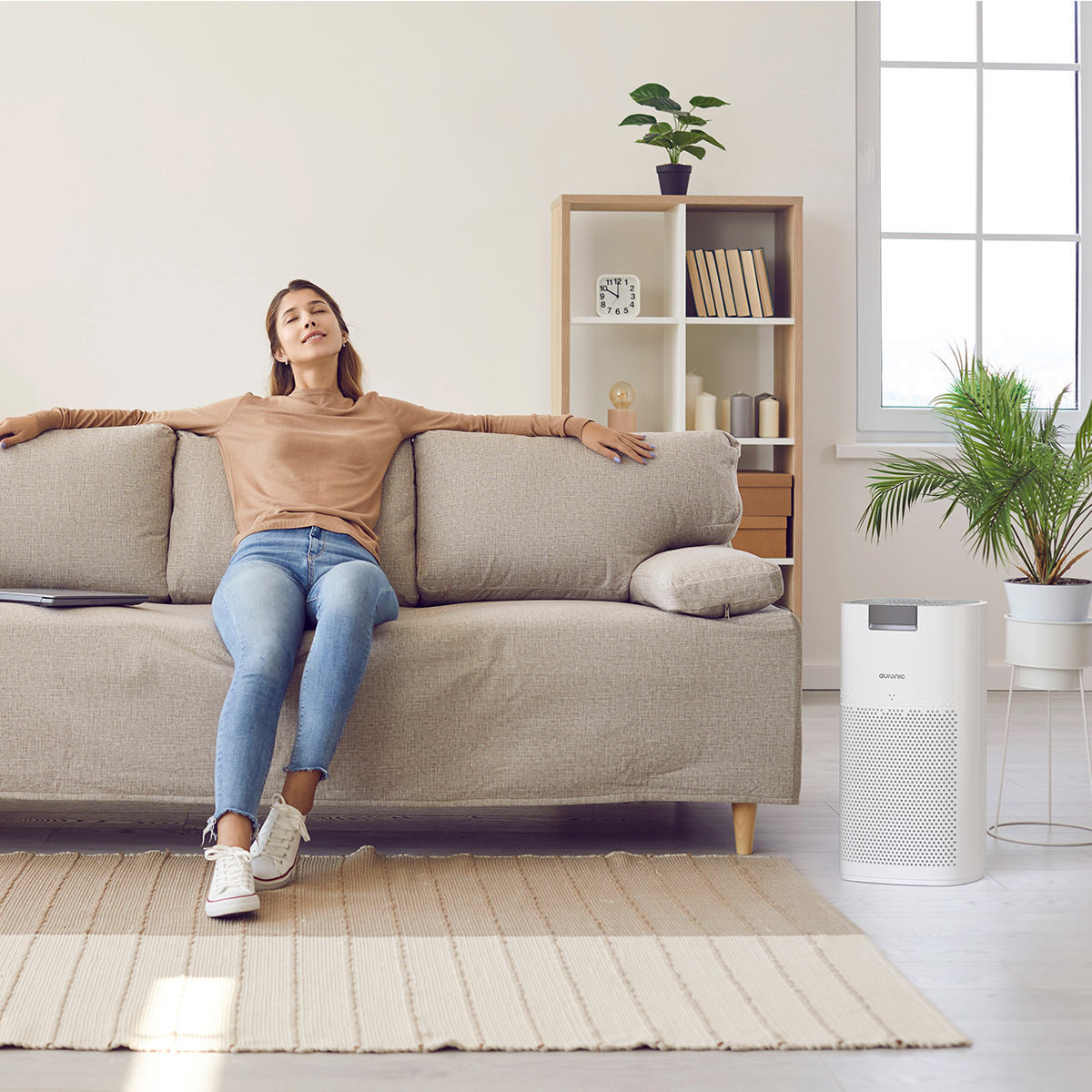 Eine Frau entspannt sich auf einem Sofa, ein Luftreiniger steht daneben.