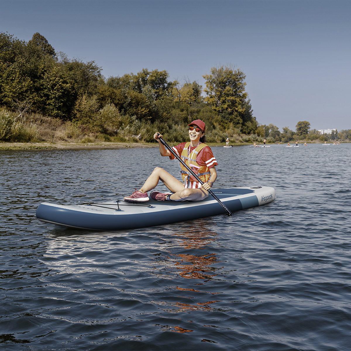 Woman in red shirt, life vest, and cap paddleboards on a blue and white board.