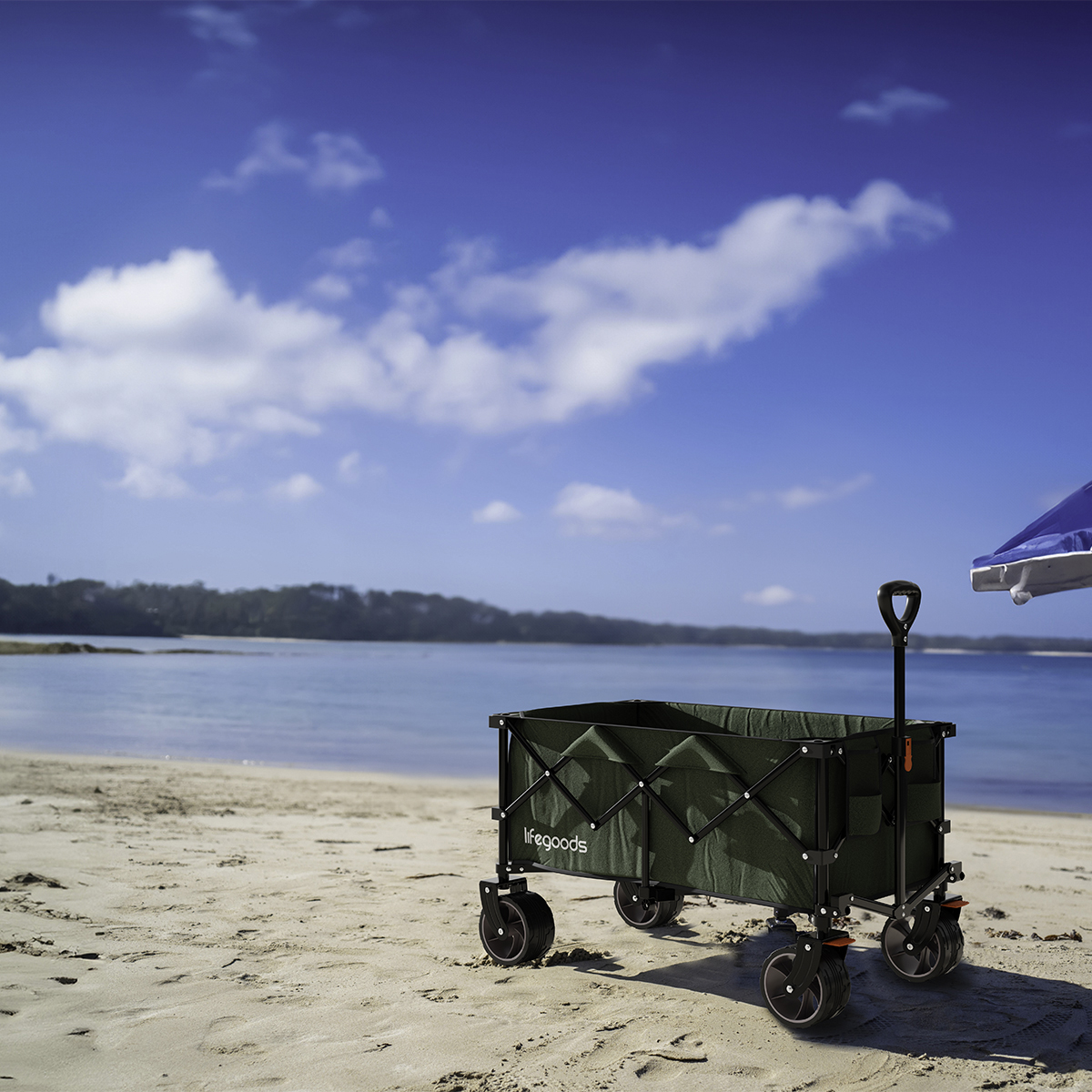 A green wagon sits on a sandy beach near the ocean under a blue sky with clouds.