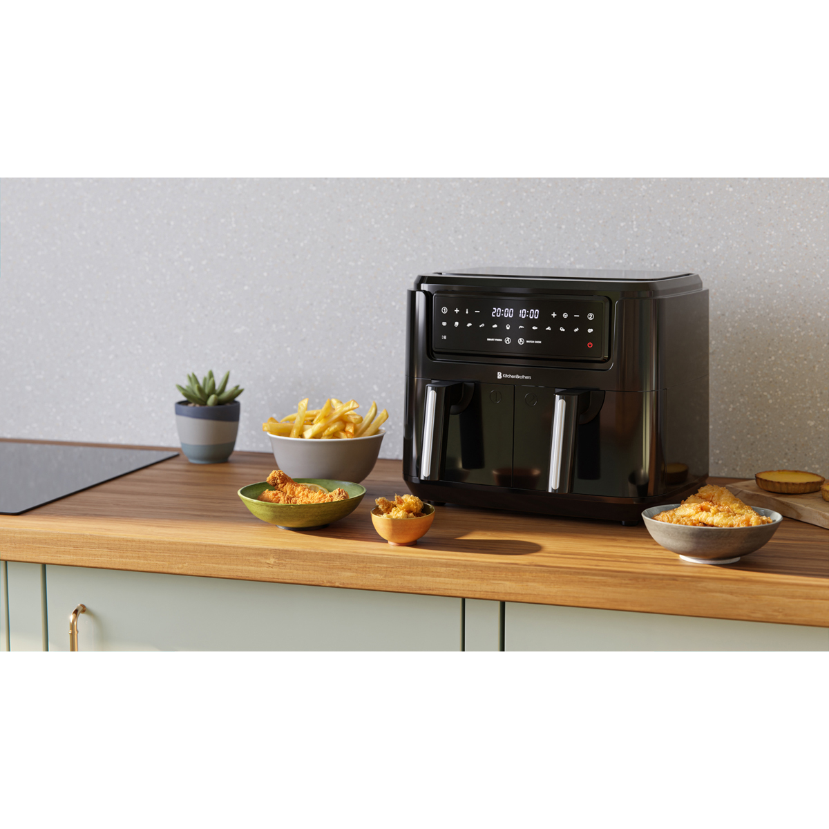 A black double air fryer on a wooden countertop with bowls of fries, chicken, and snacks.