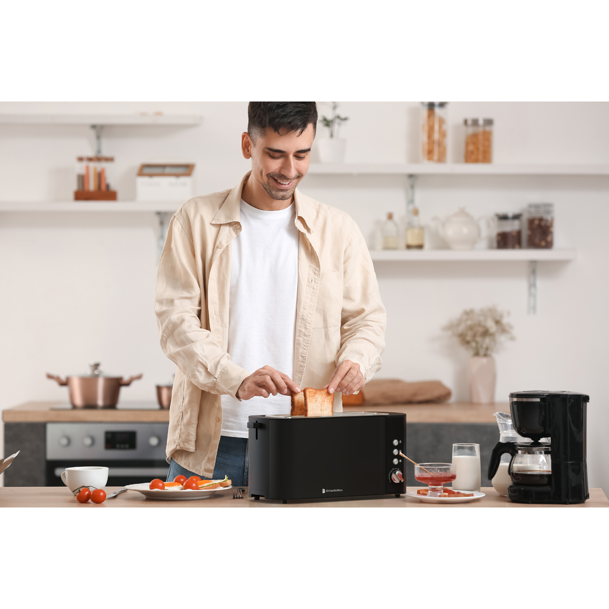 Man places toast in black toaster; coffee, milk, and jam nearby.