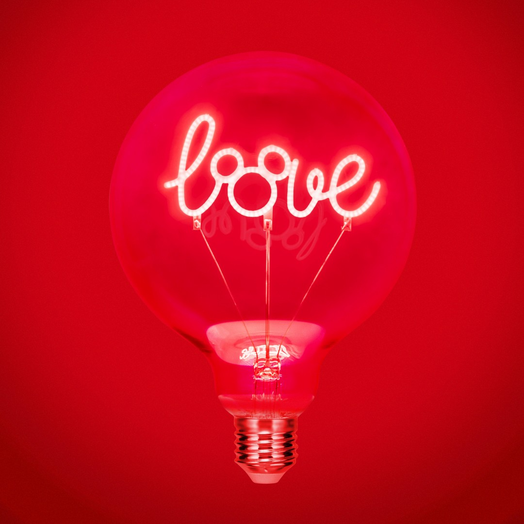 Una lampadina rossa con la parola "amore" illuminata al neon bianco su sfondo rosso.