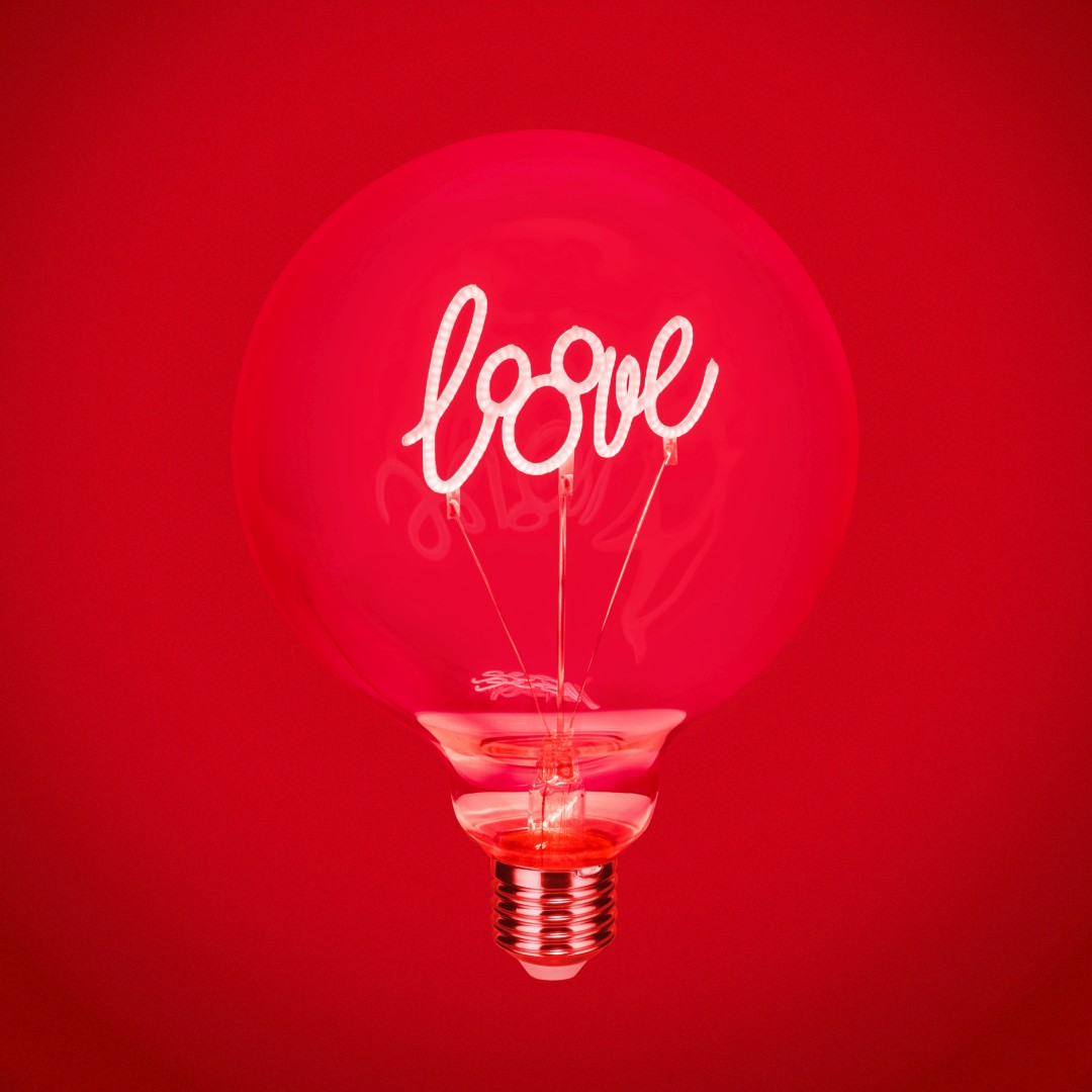 Una lampadina con la parola "amore" in luce al neon su sfondo rosso.
