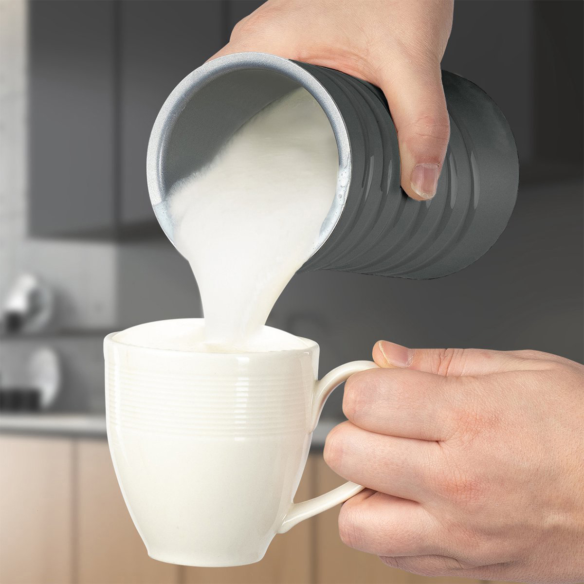 Milch wird aus einem grauen Krug in eine weiße Tasse gegossen.
