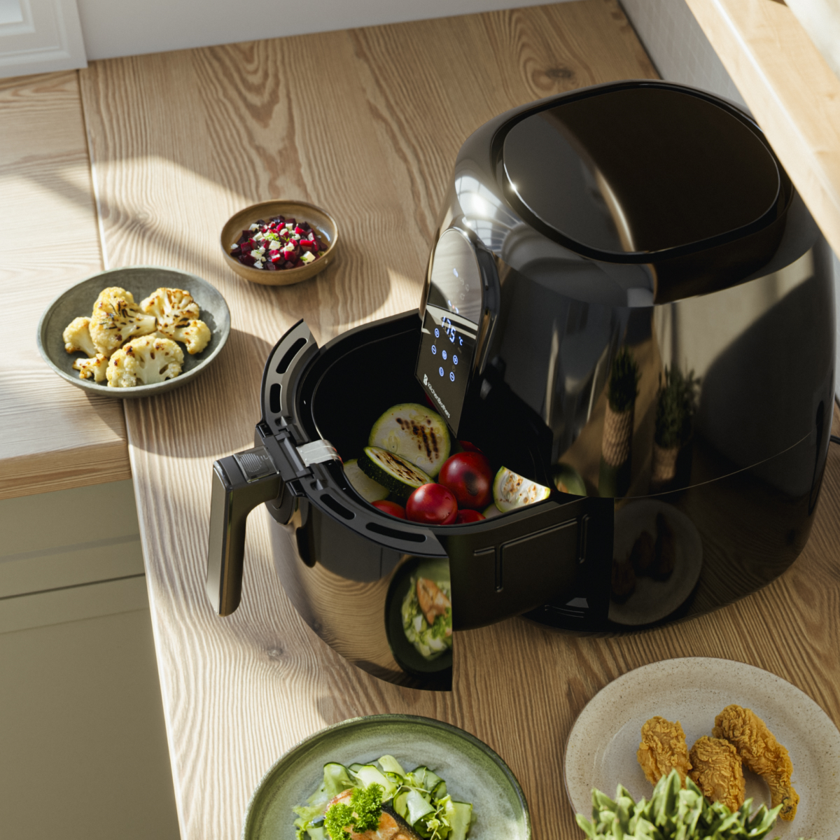 A black air fryer with vegetables and cooked cauliflower on a wooden counter.