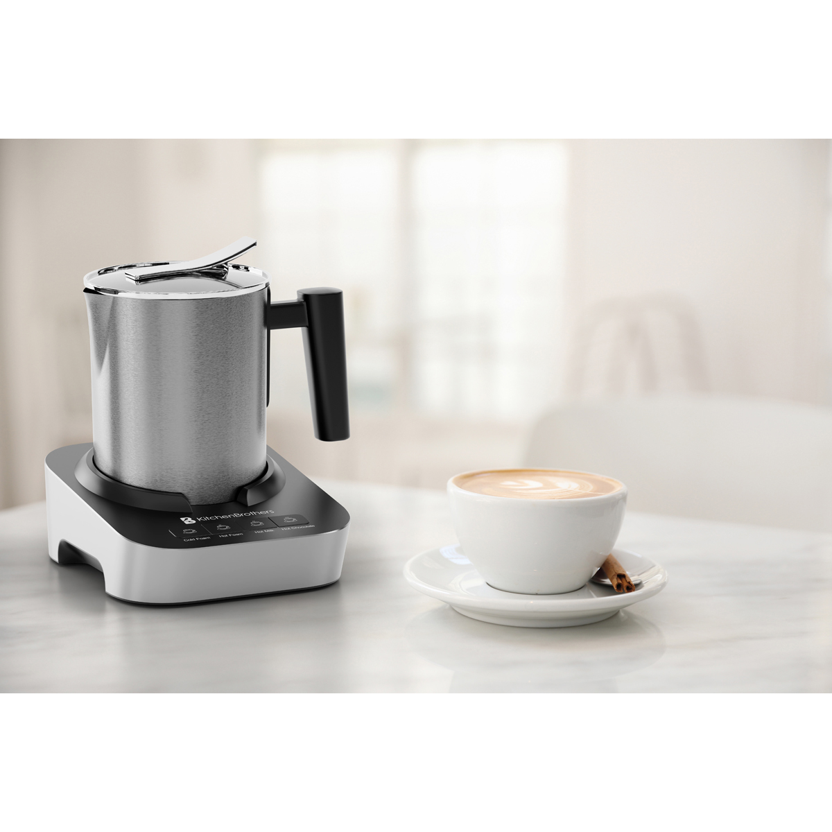 Silberner Milchaufschäumer mit schwarzem Griff neben einer Tasse Cappuccino auf einem Tisch.