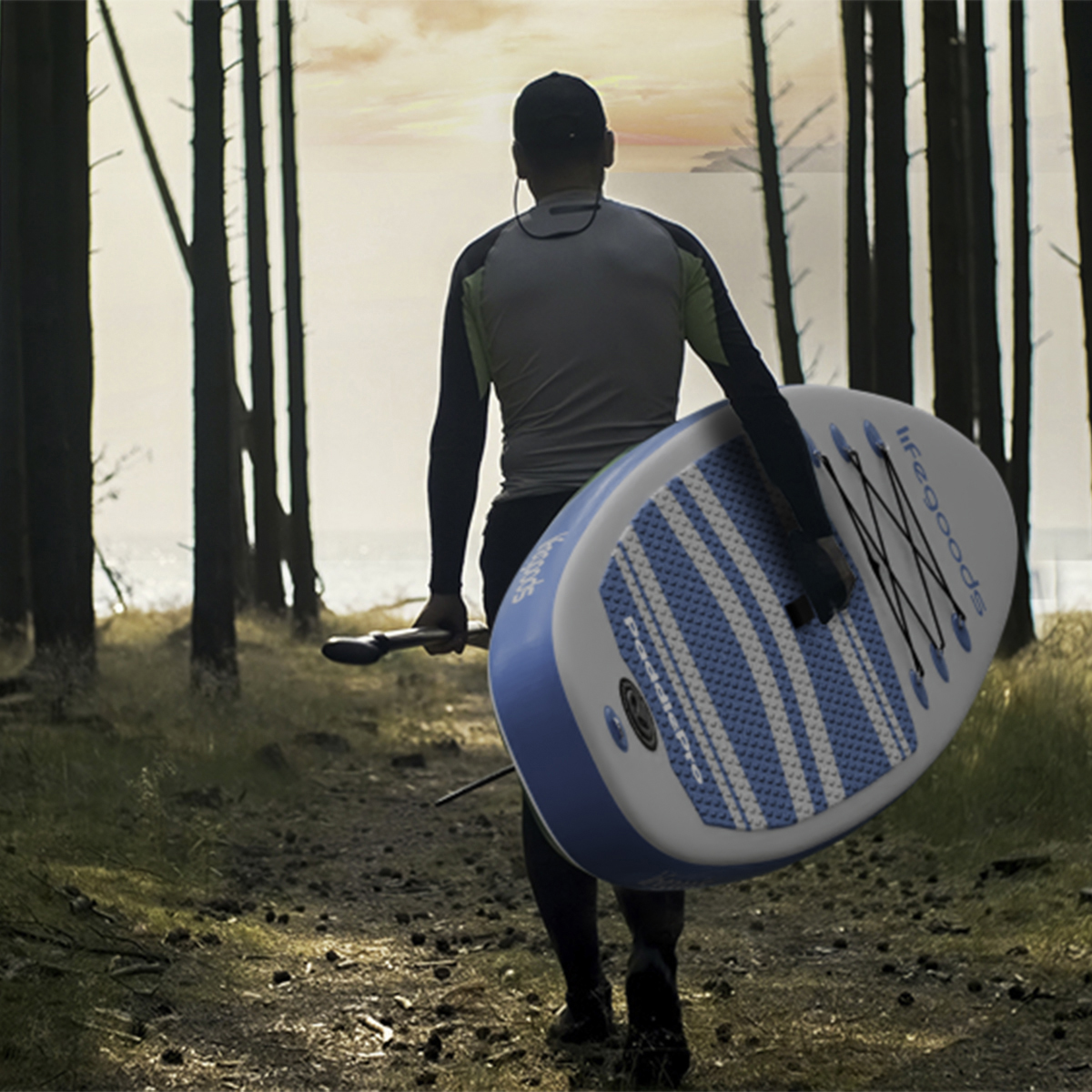 Man loopt met paddleboard en peddel door een bos naar het water.