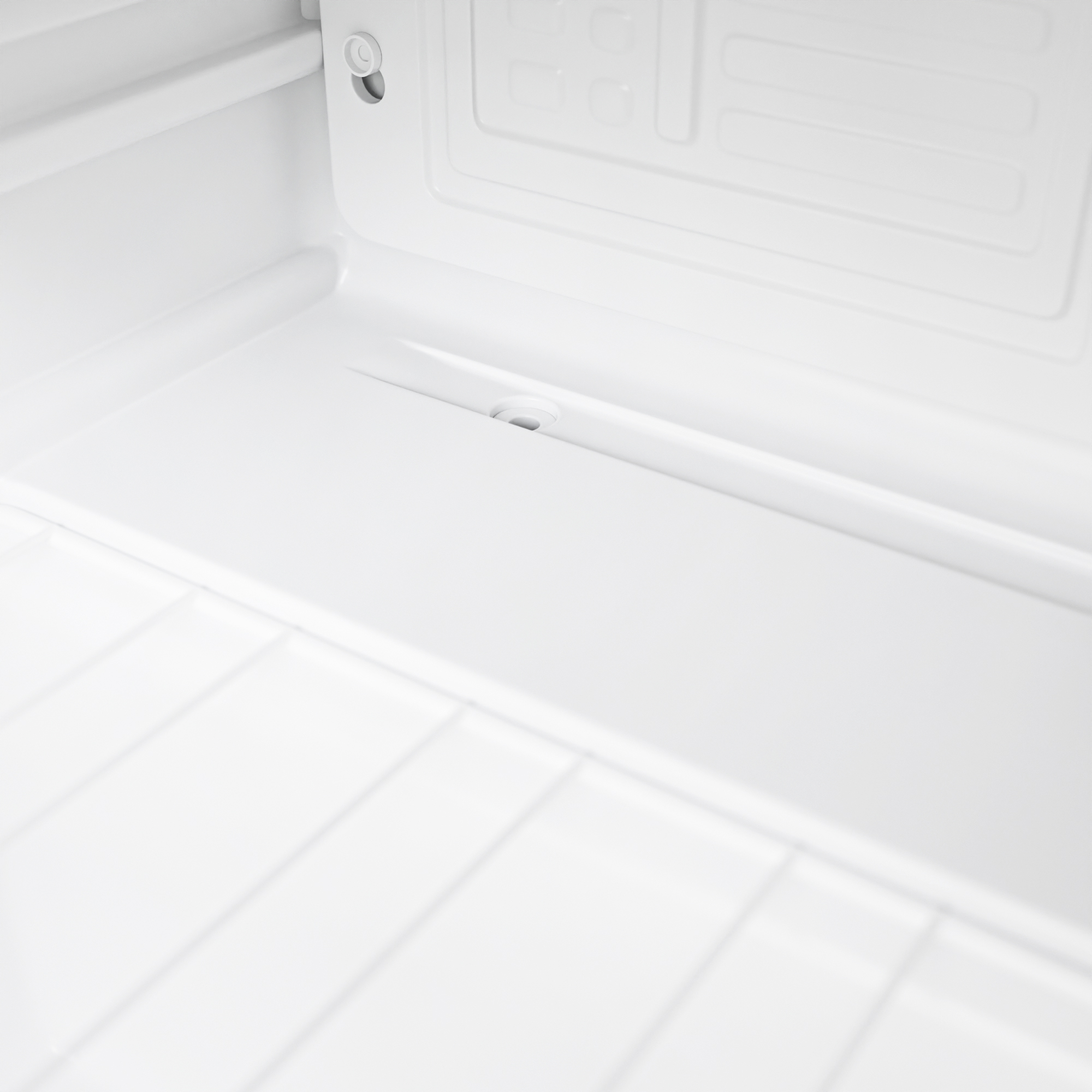 Interieur van een witte koelkast met ribbels en een klein afvoergaatje.