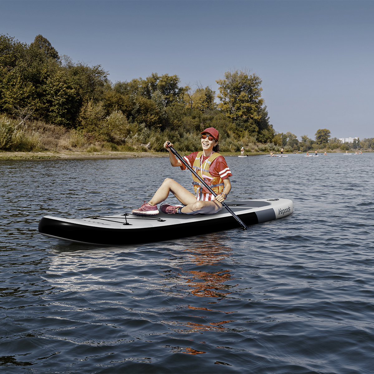 Eine Frau sitzt auf einem Paddleboard und hält ein Paddel. Bäume und Himmel im Hintergrund.