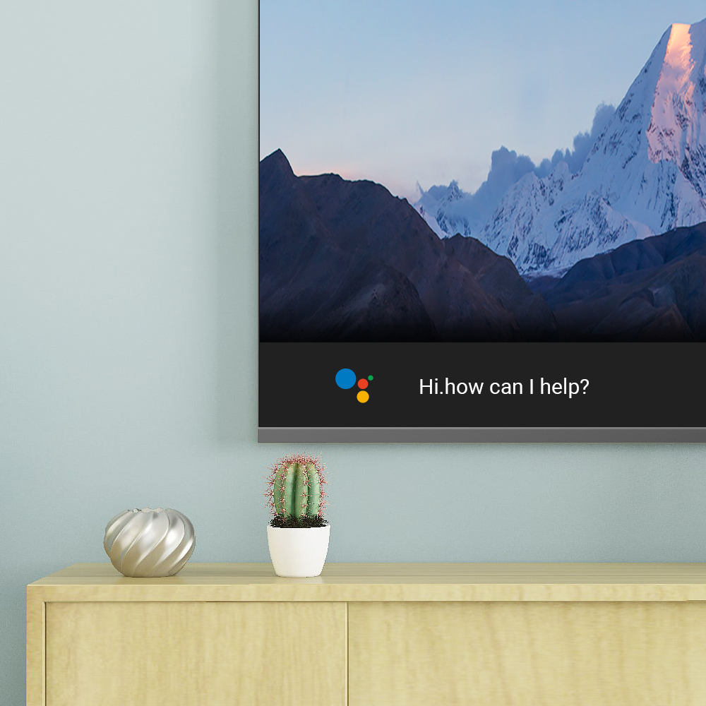 A television displays a mountain panorama and the Google Assistant prompt.