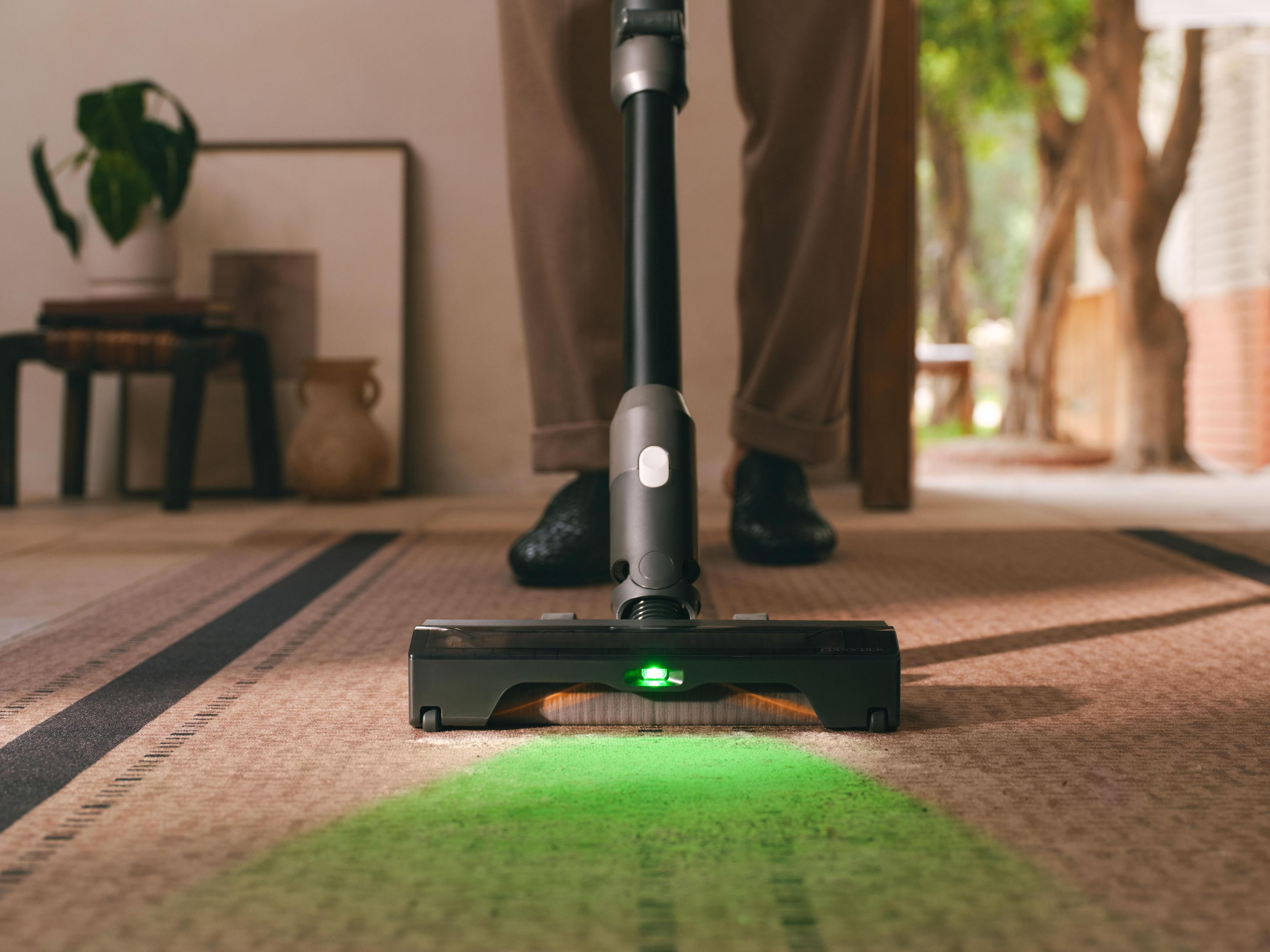Un aspirapolvere con luci LED verdi pulisce un tappeto.