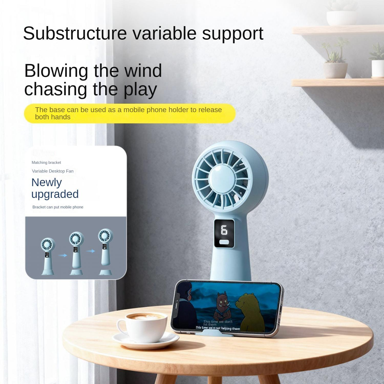 Ein blauer Ventilator mit digitaler Anzeige steht auf einem Tisch, daneben ein Handy mit Cartoon.