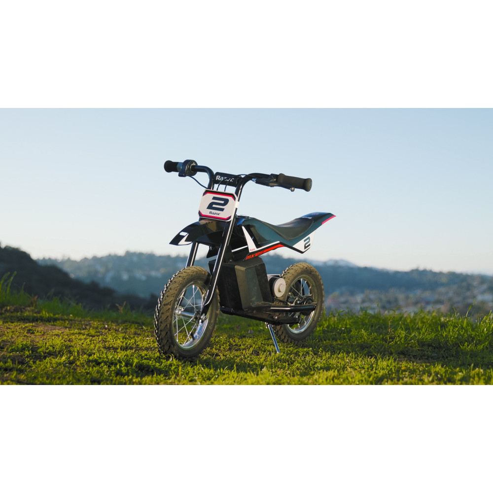 Czarny elektryczny motor crossowy z numerem 2 z przodu, stoi na trawiastym terenie ze wzgórzami.