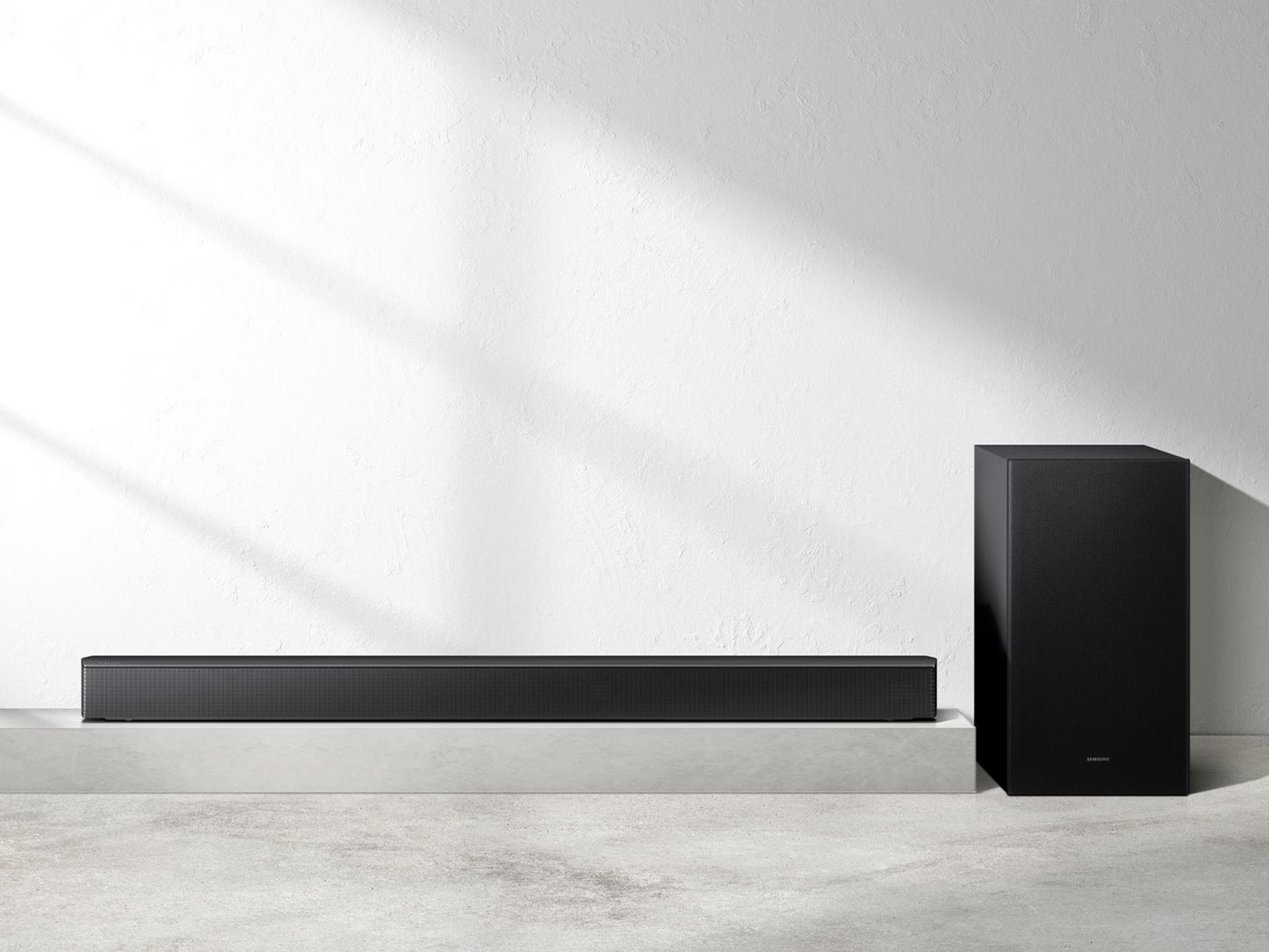 Schwarzer Soundbar und Subwoofer auf einem grauen Podest vor weißer Wand.
