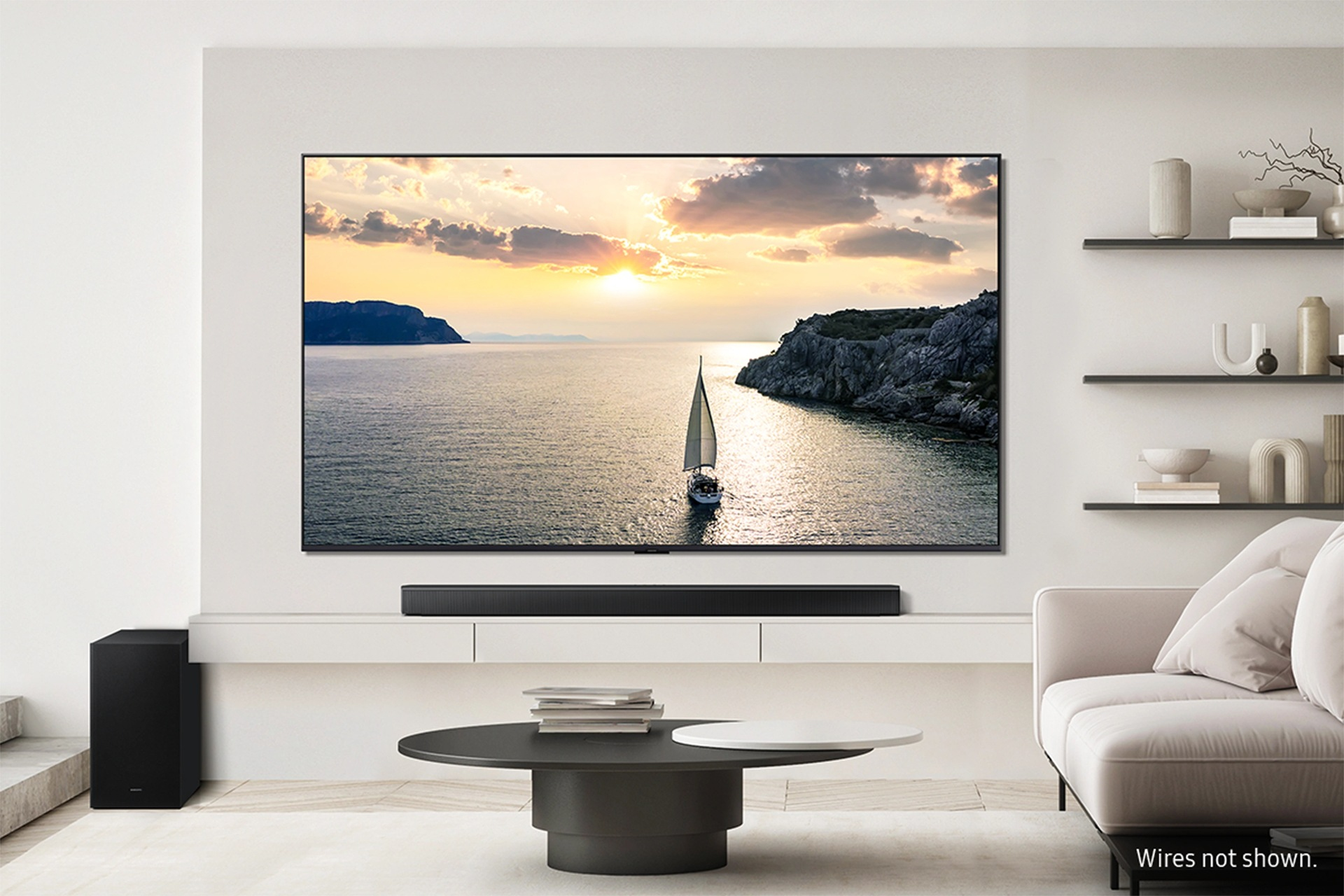 Żaglówka na morzu o zachodzie słońca, ze skalistymi klifami i chmurami. Telewizor i soundbar na pierwszym planie.