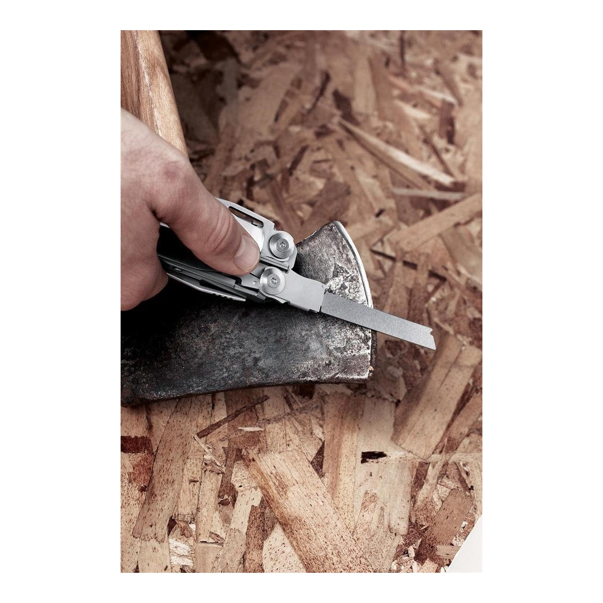 Eine Hand benutzt ein Multitool, um eine Axt auf einem Holzuntergrund zu schärfen.