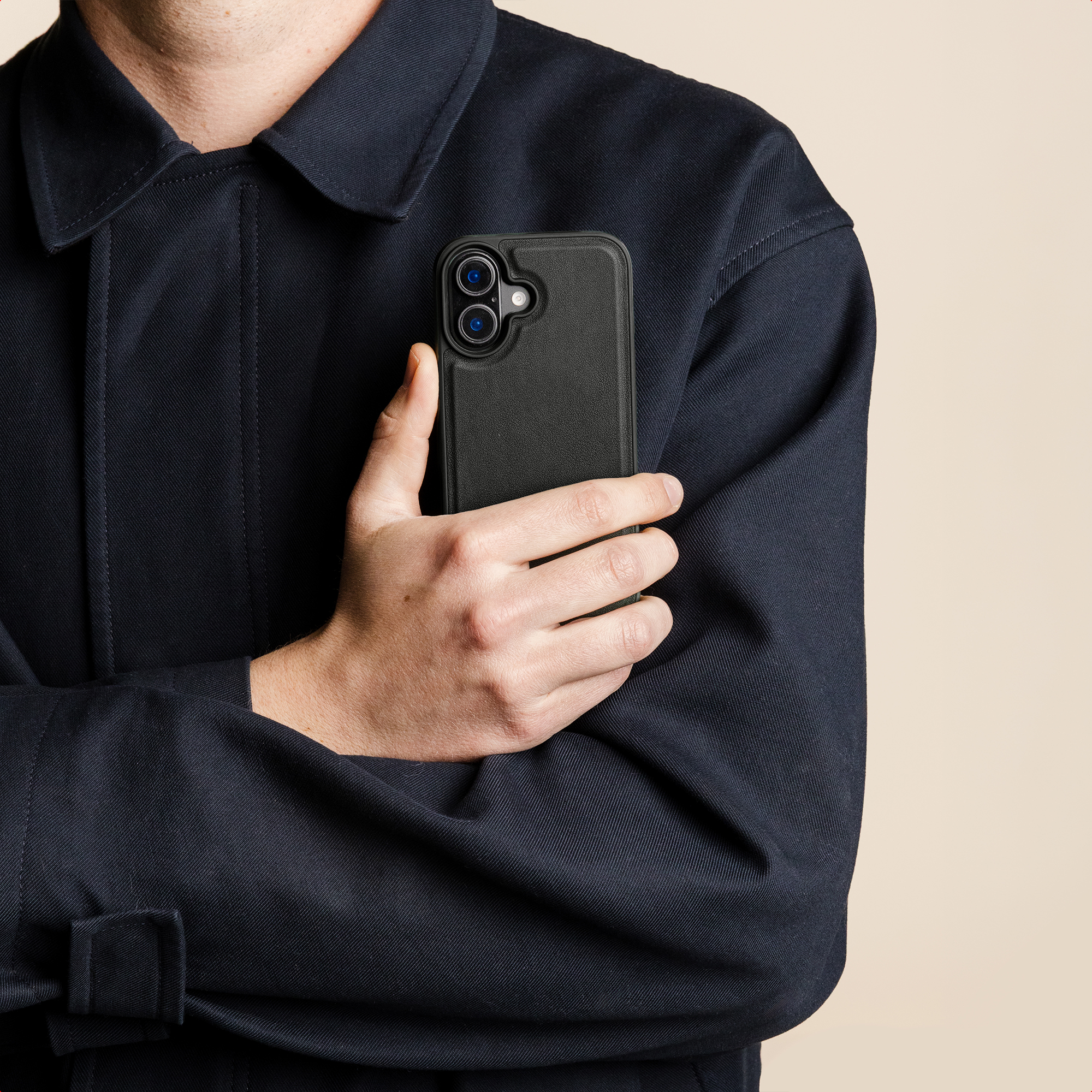Man in donkerblauw jasje houdt zwarte telefoon met dubbele camera vast.
