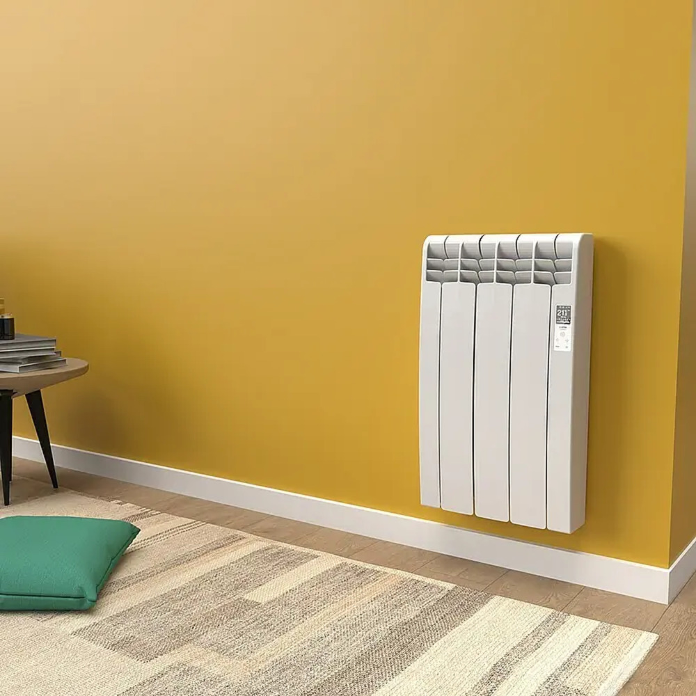 Un radiador blanco en una pared amarilla sobre una alfombra con un cojín.
