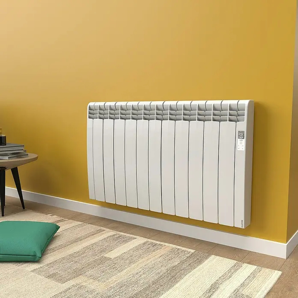 Un radiador blanco montado en una pared amarilla, con alfombra y mesa.