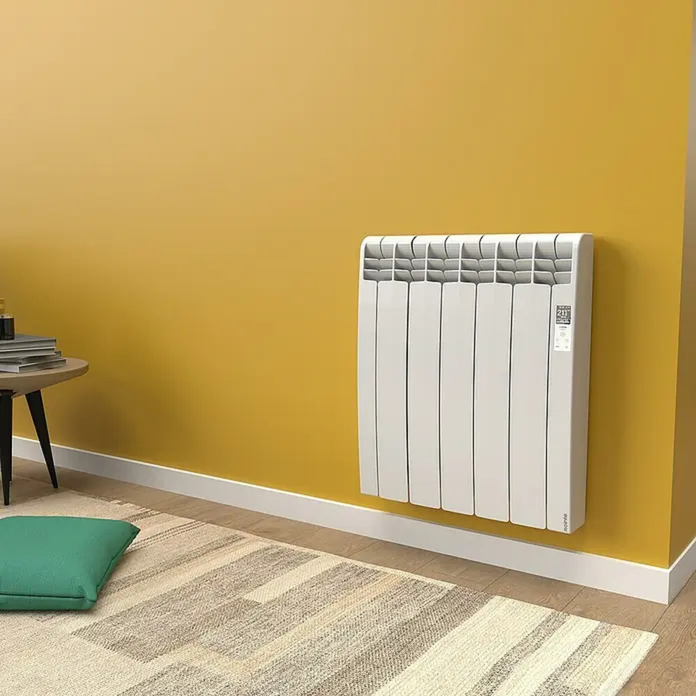 Un radiador blanco en una pared amarilla, con alfombra y cojín.