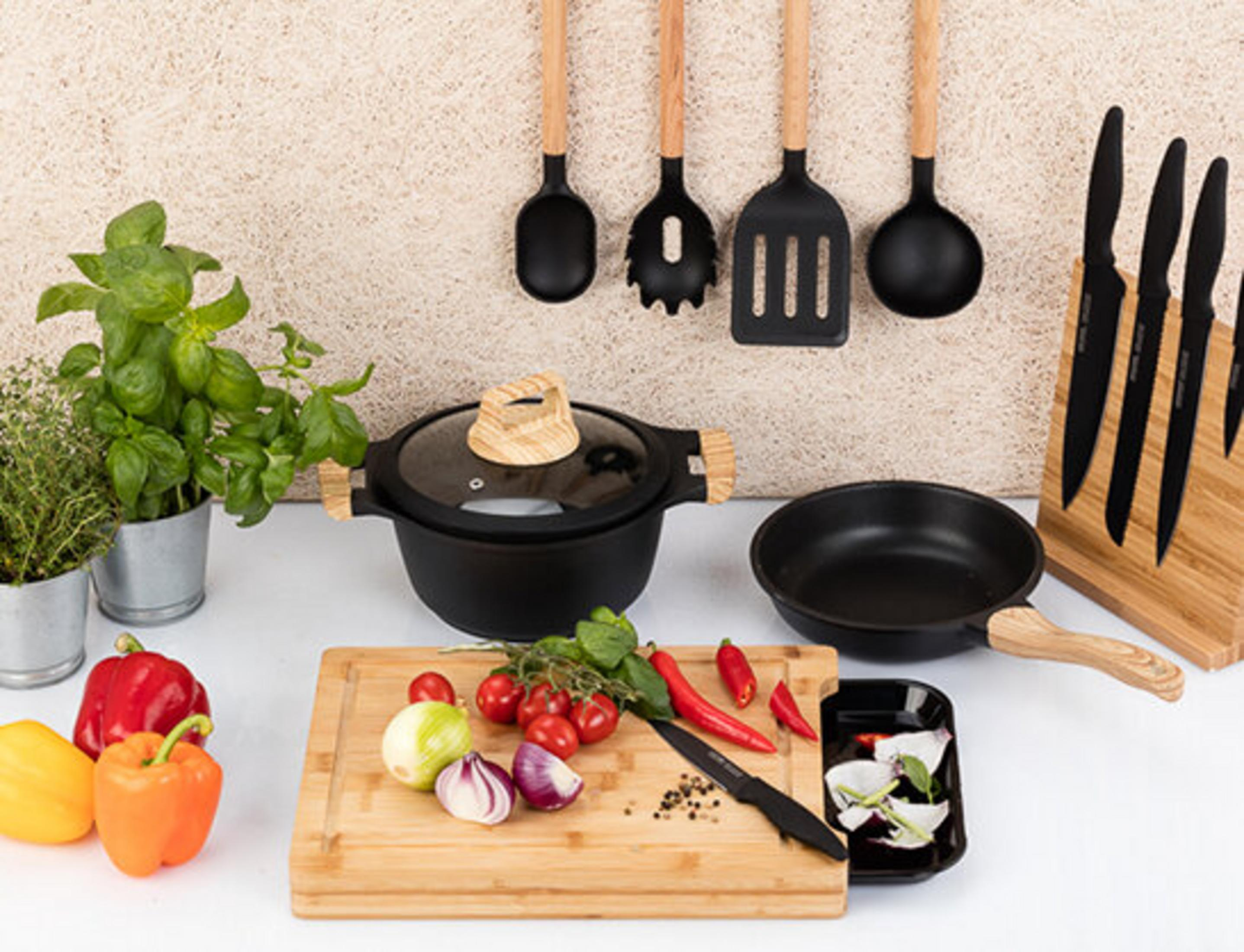 Utensilios de cocina y verduras, incluyendo una olla, sartén, tabla de cortar con cebollas y tomates.