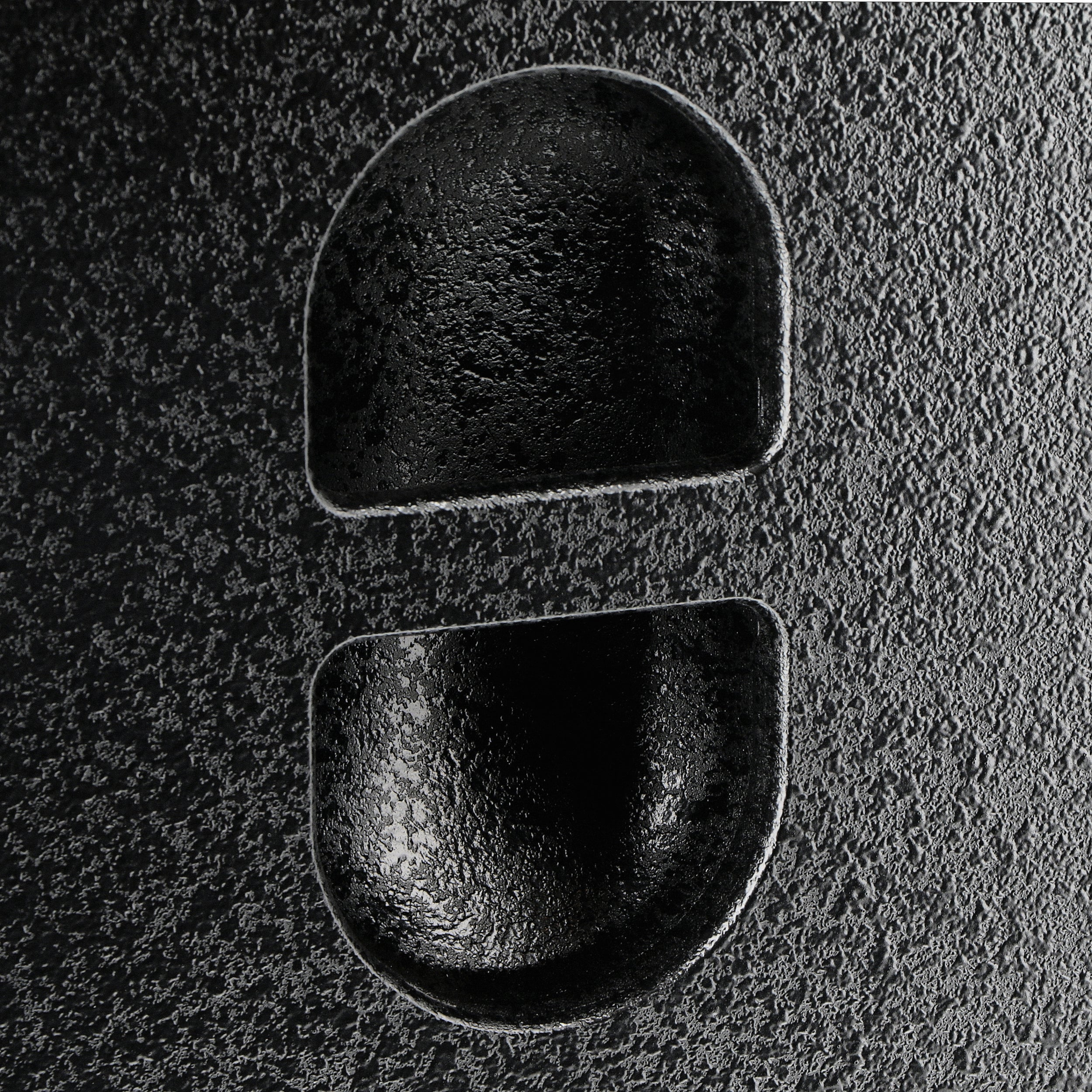 Two black, shiny indentations on a textured dark surface.