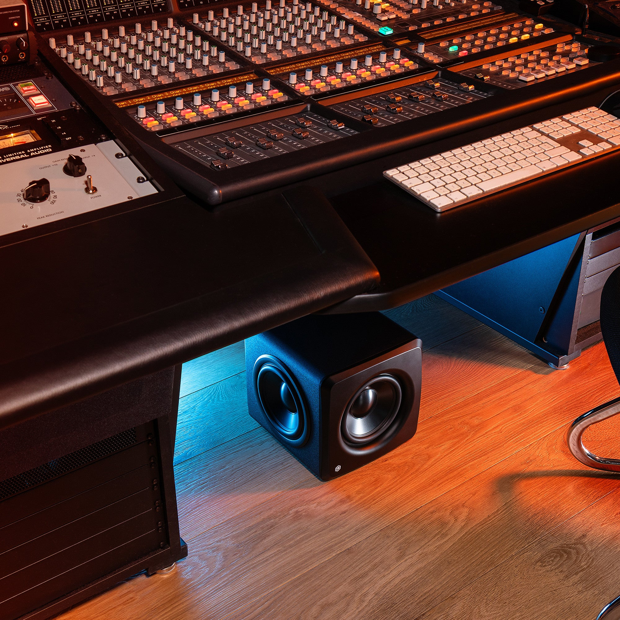 Una console di missaggio con luci e manopole, una tastiera accanto. Un subwoofer sotto.