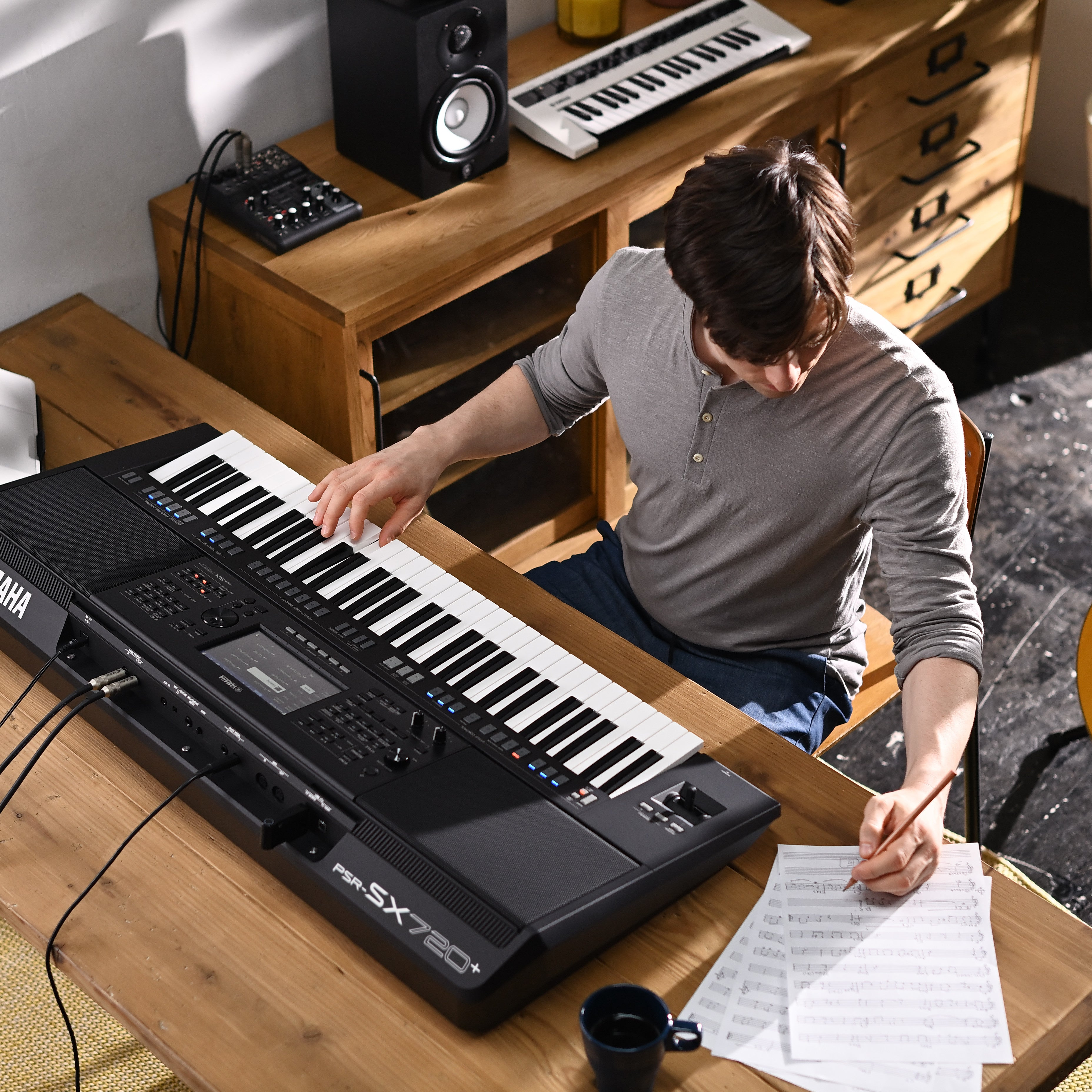 Man speelt keyboard met bladmuziek en potlood op houten tafel.