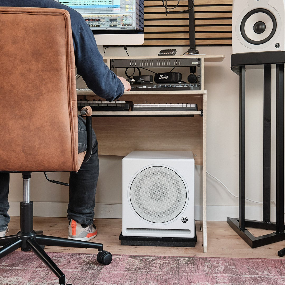 Man sits at a desk with music equipment, a white subwoofer, and speaker.