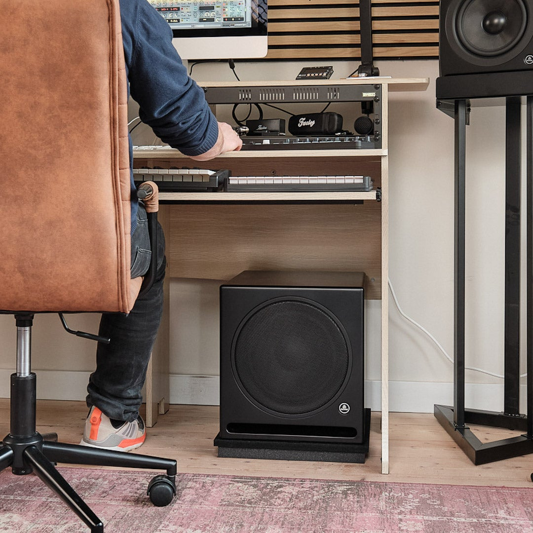 Person at desk with keyboards, computer, and subwoofer. Speaker on stand.