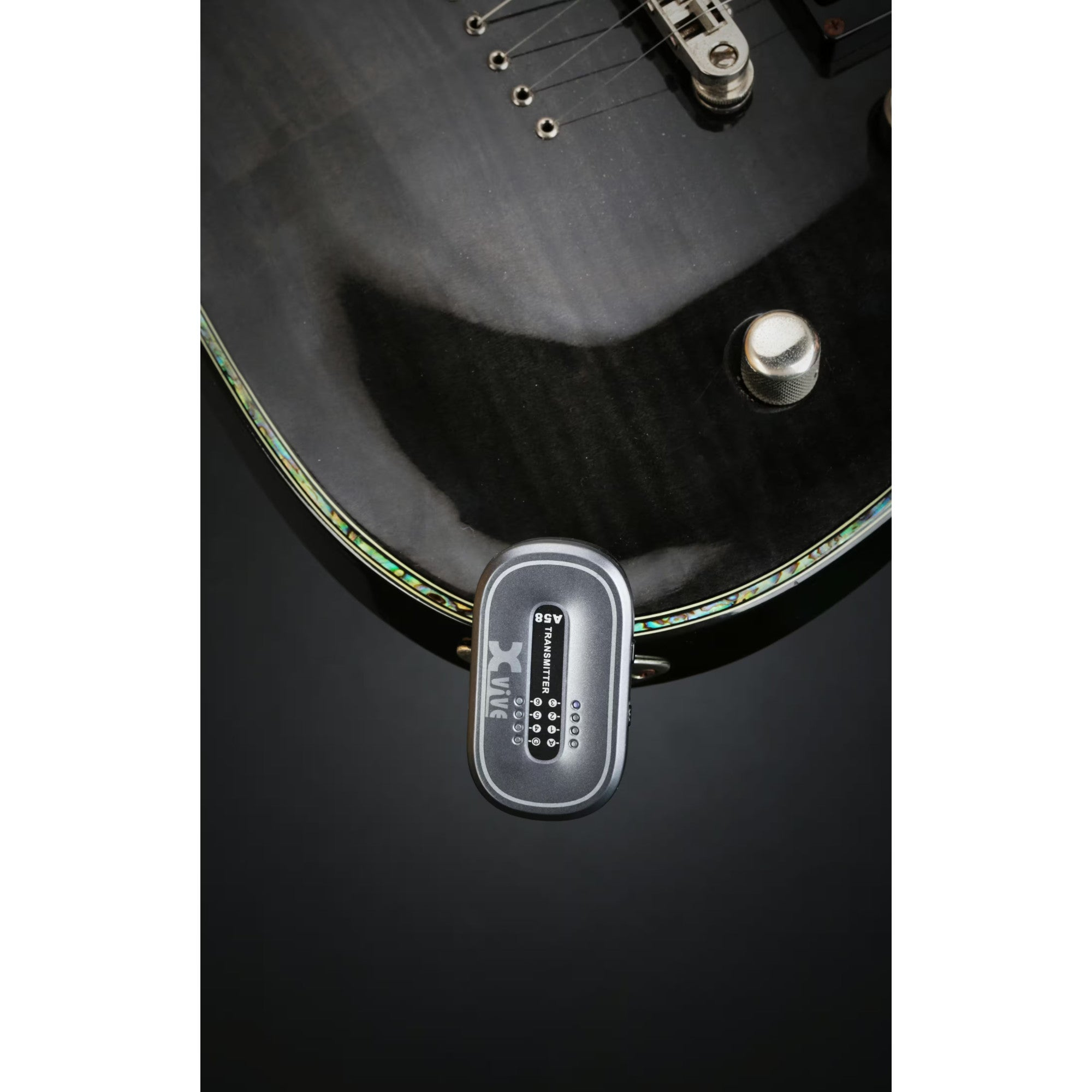A silver wireless transmitter is attached to a black electric guitar.