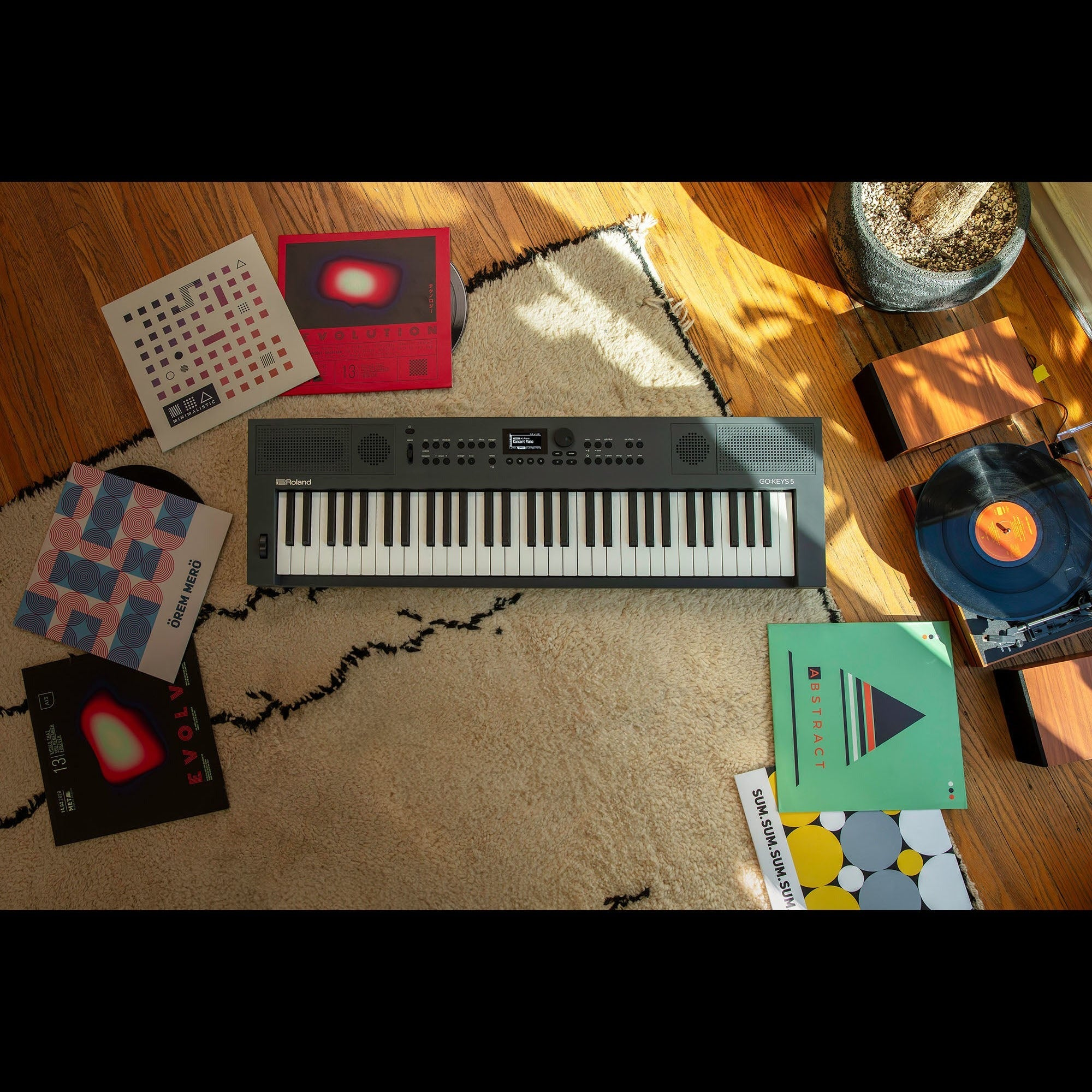 Een Roland keyboard ligt op een kleed, omringd door vinylplaten en een platenspeler.