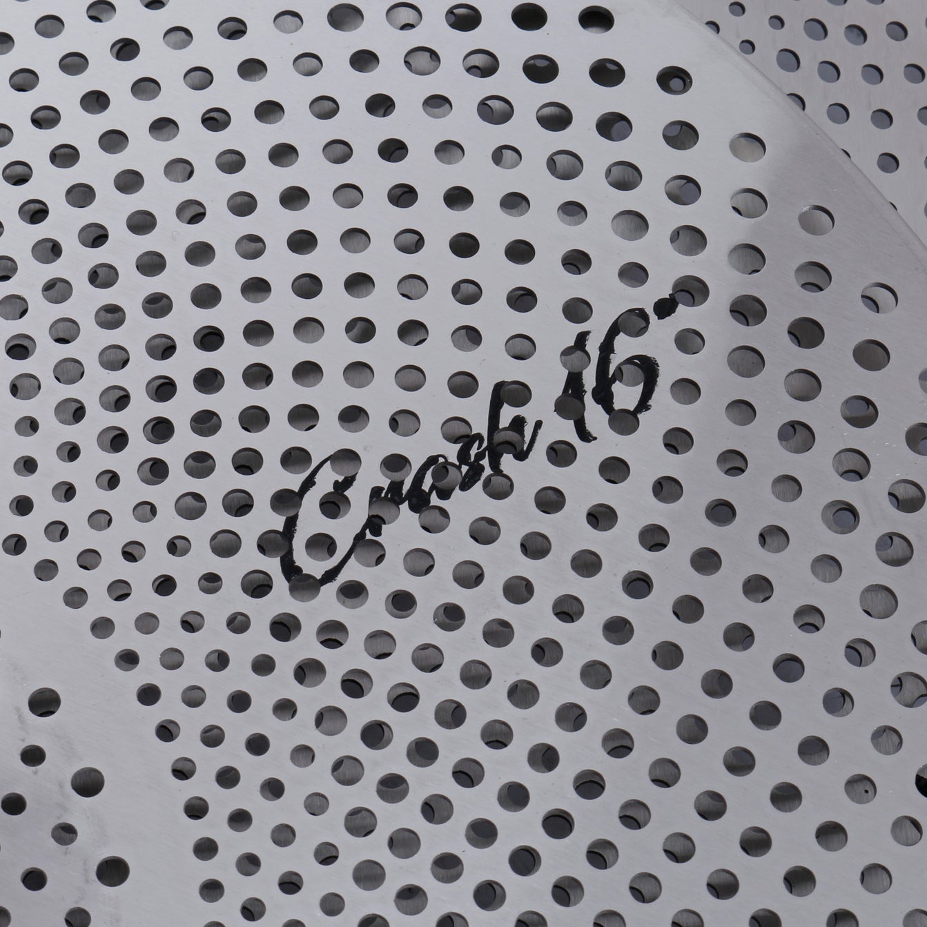 Close-up of a cymbal with a perforated pattern and black text "Crash 16".