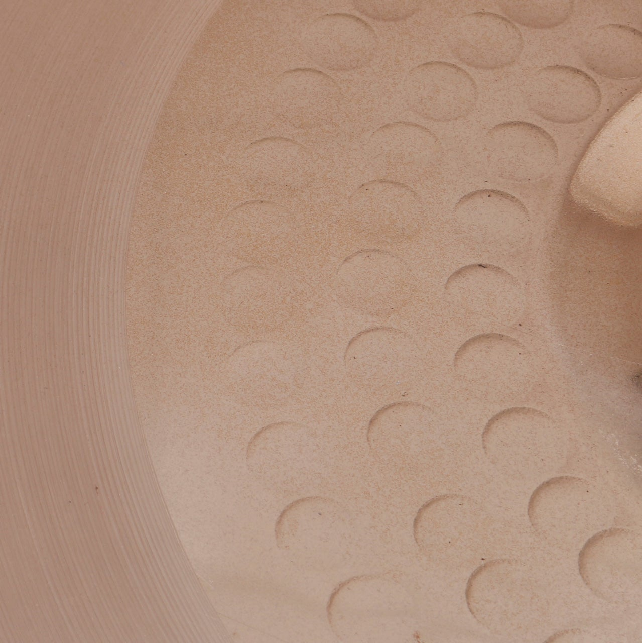 A close-up of a light brown ceramic surface with embossed circle patterns and vertical grooves.