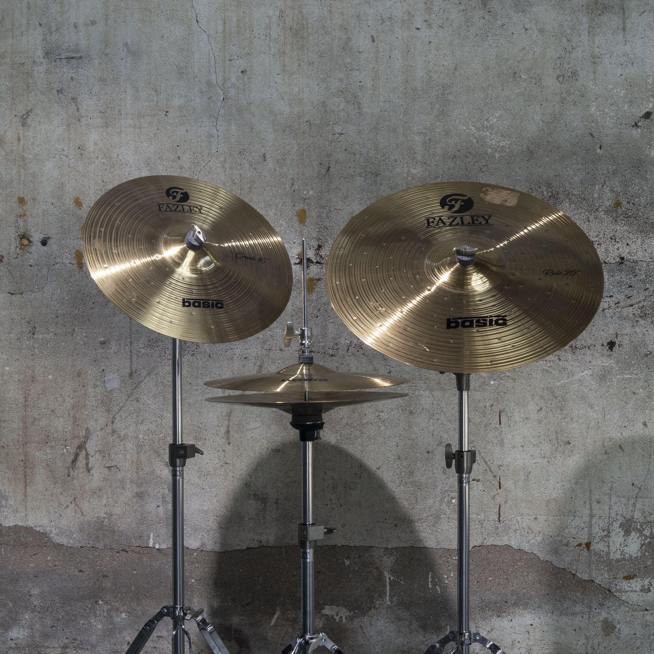 Three golden cymbals on stands against a concrete wall.