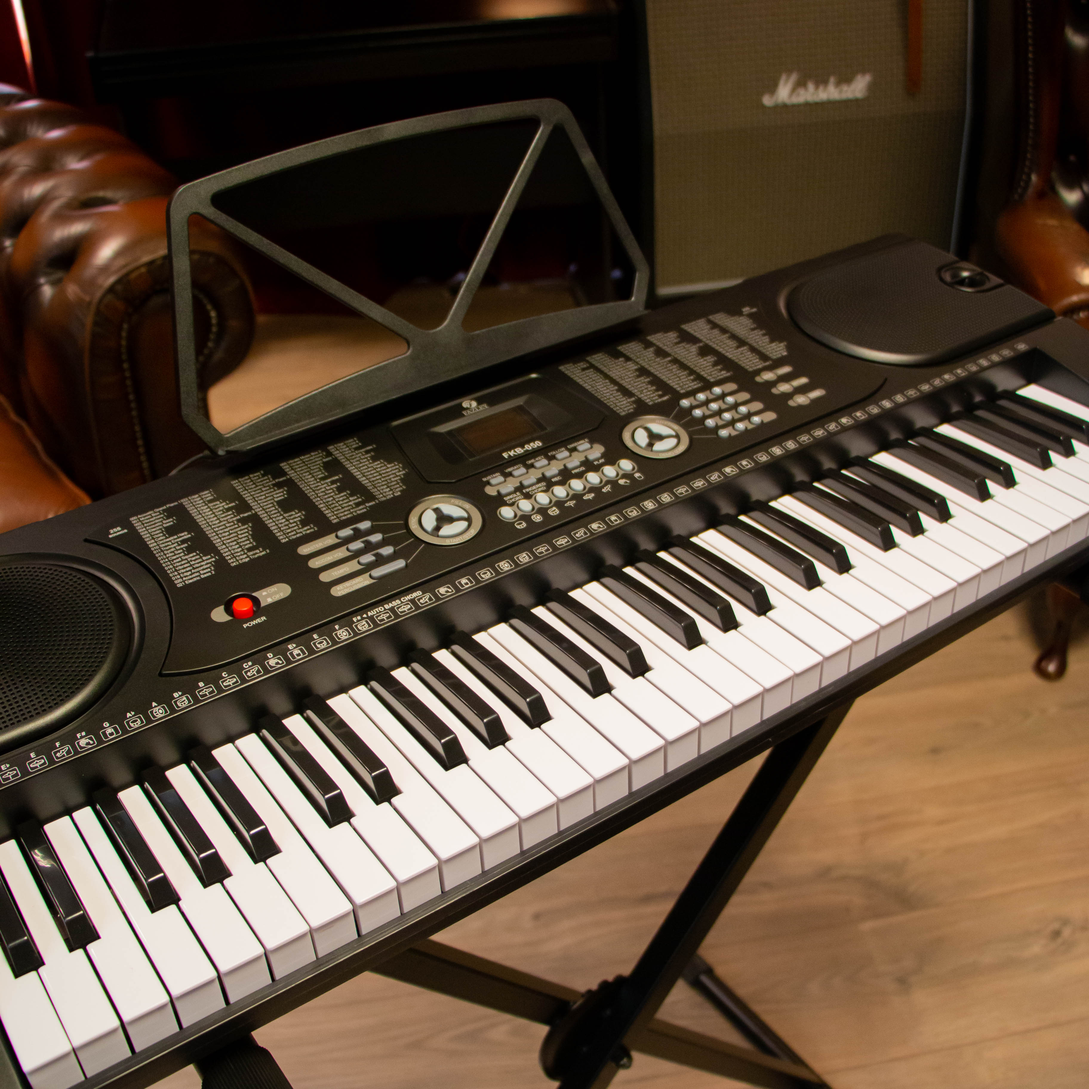 Een zwart keyboard op een standaard, voor bruine lederen stoelen en een Marshall versterker.