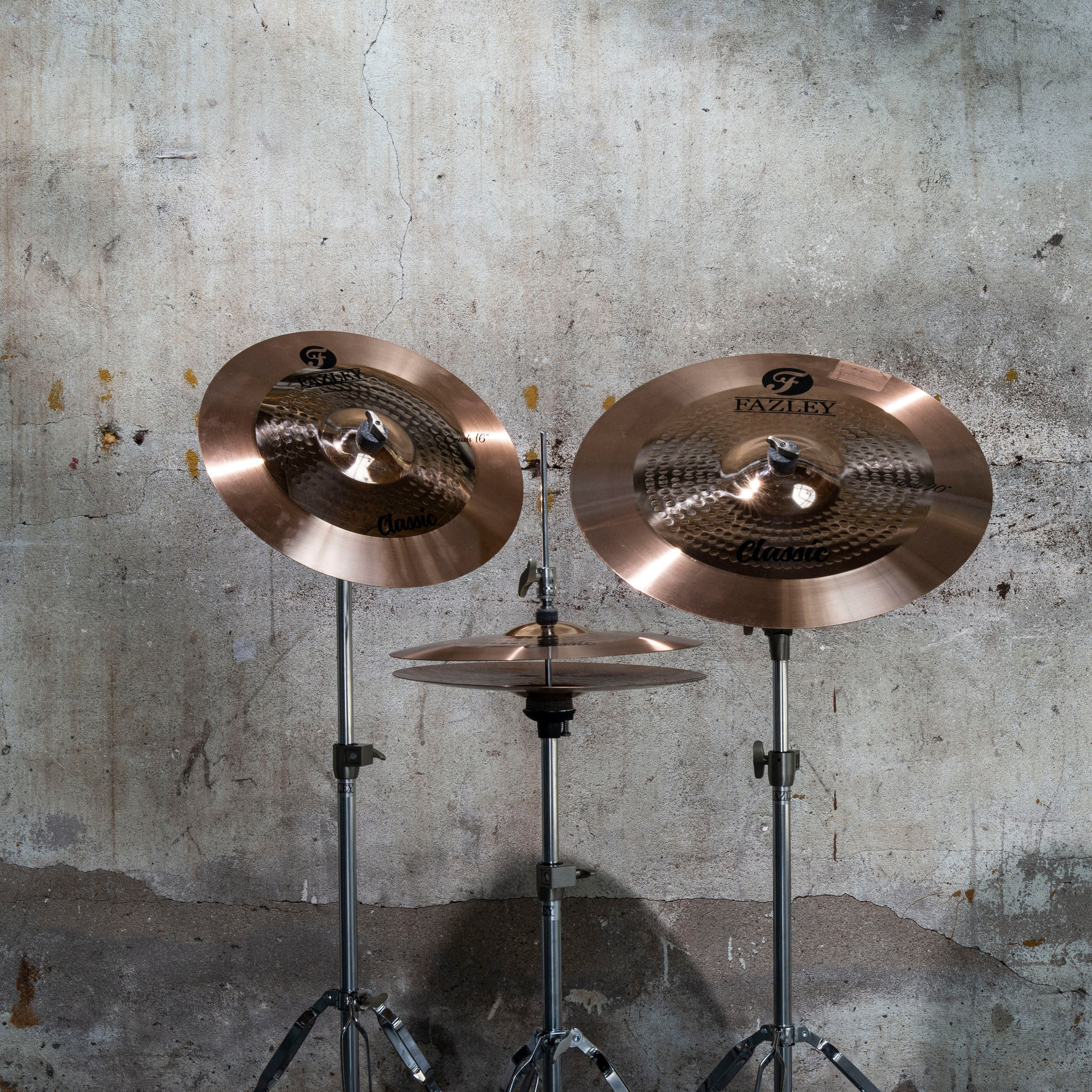 Three brass cymbals on stands in front of a concrete wall.