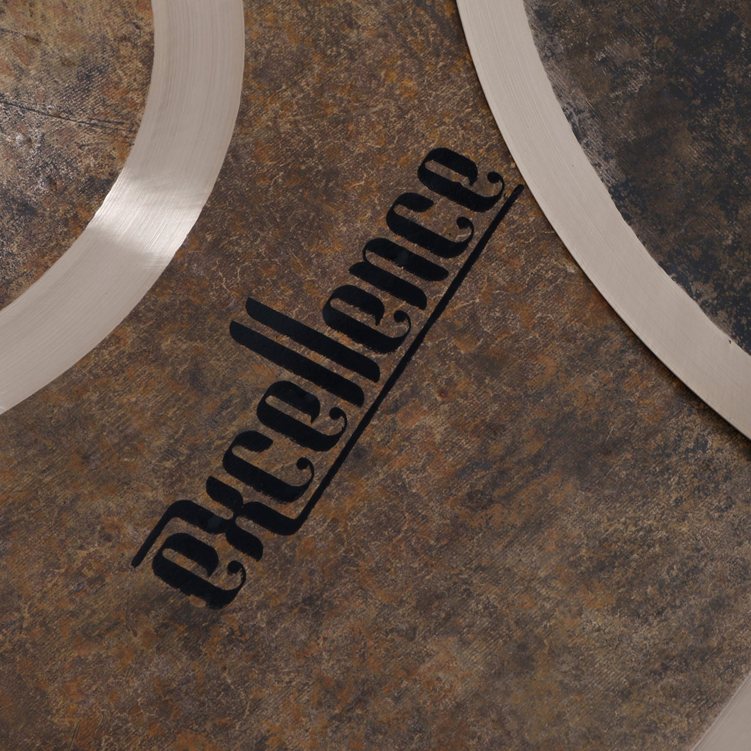 Close-up of a metallic object with the word Excellence in black script. Textured brown background.