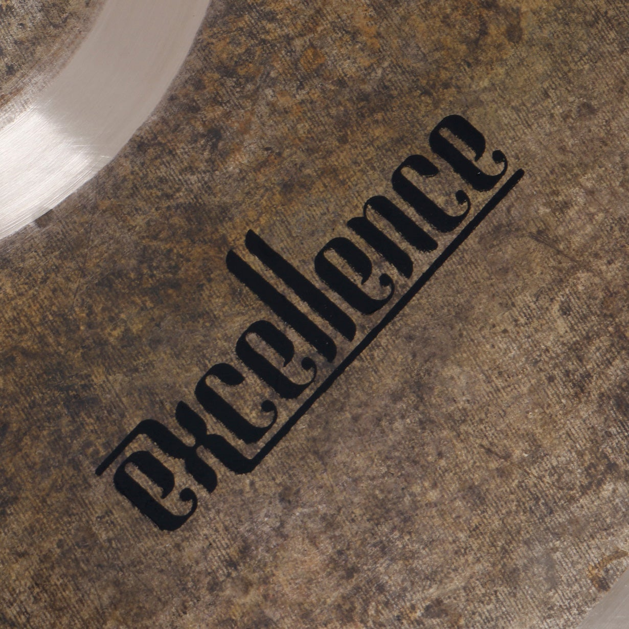 Black text "Excellence" on a weathered, stone-like surface with a metallic sheen.