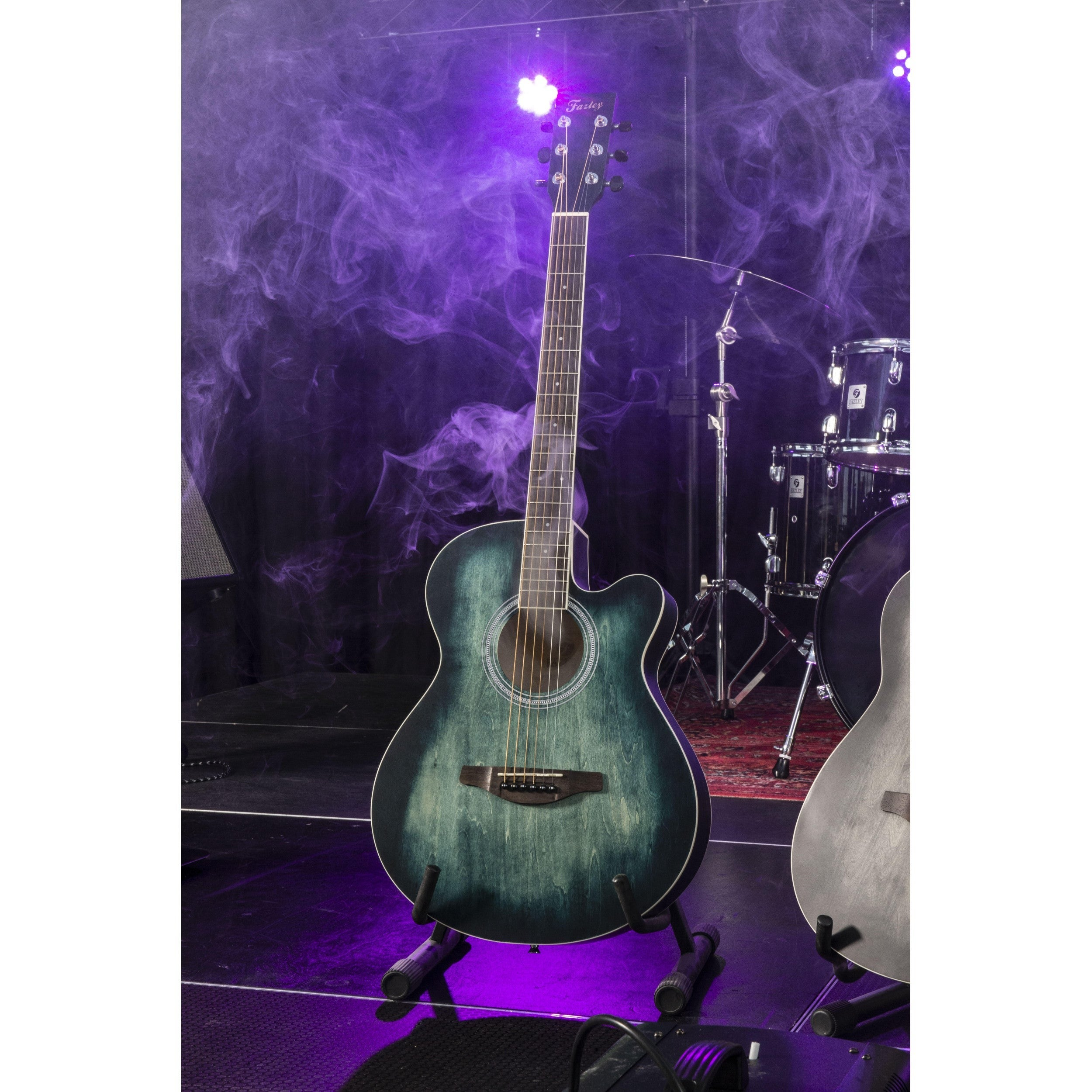 Green acoustic guitar on stand, drums and purple smoke in background.