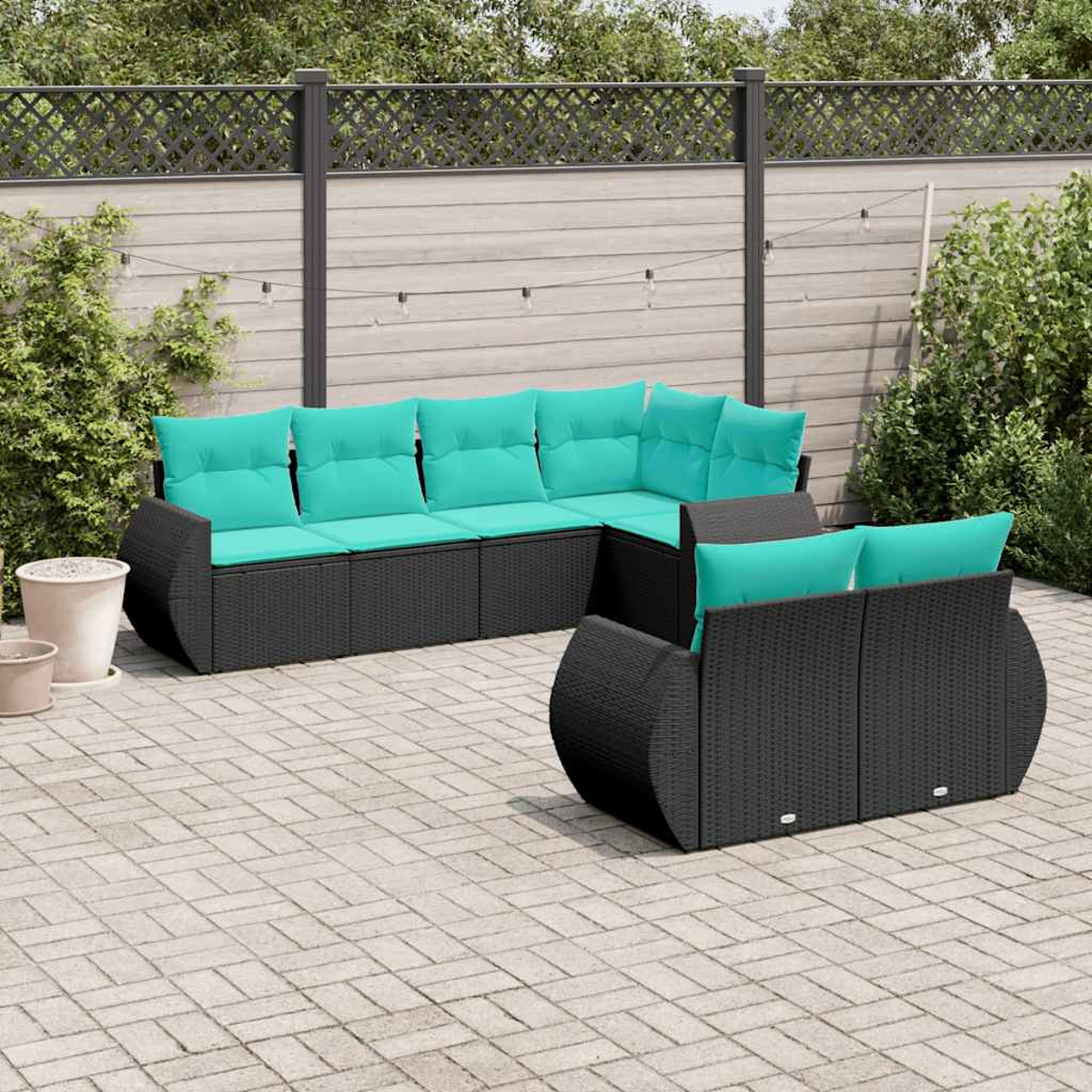 Ein schwarzes Rattan-Loungeset mit türkisfarbenen Kissen auf einer gepflasterten Terrasse.