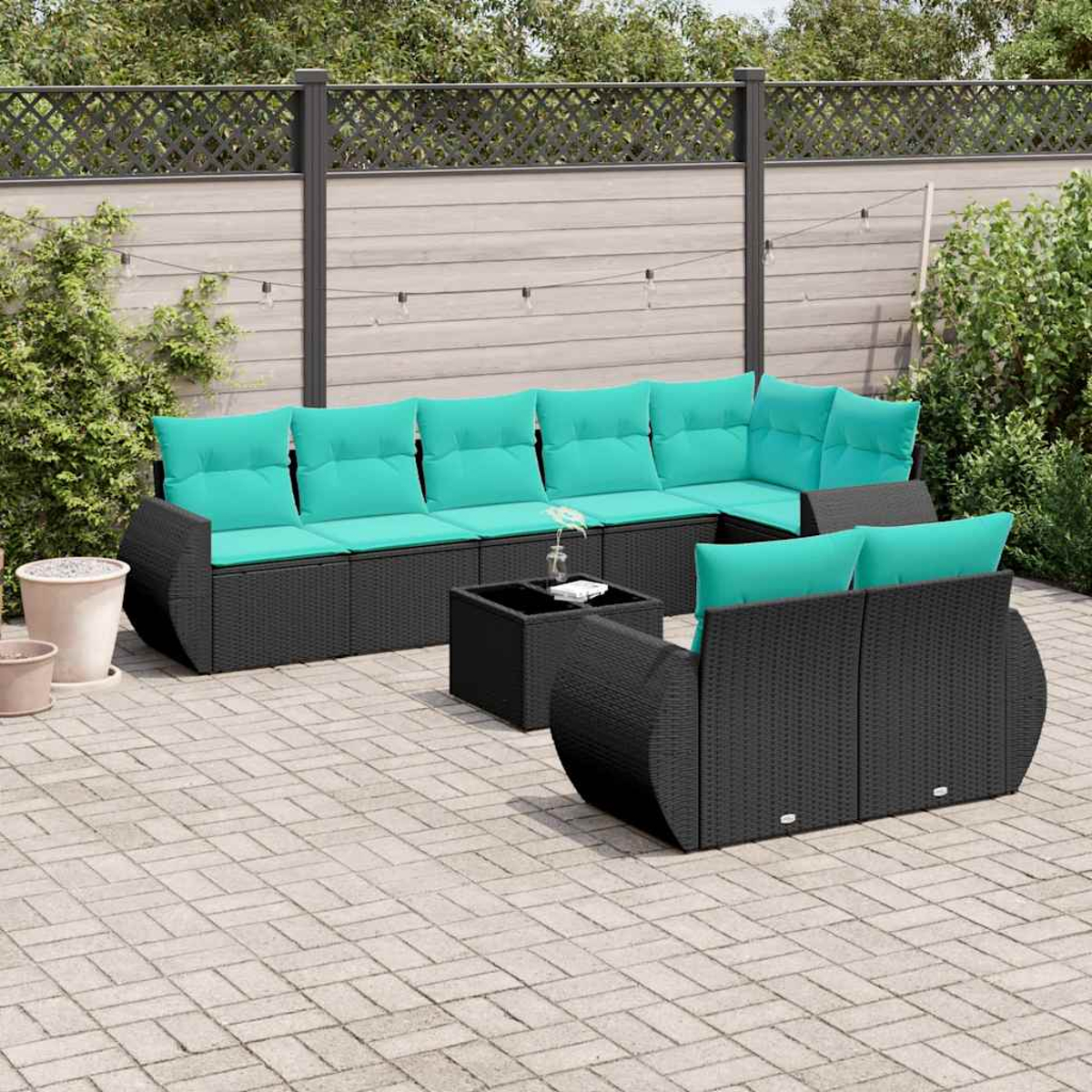 Ein schwarzes Lounge-Set mit türkisen Kissen auf einer Steinterrasse.