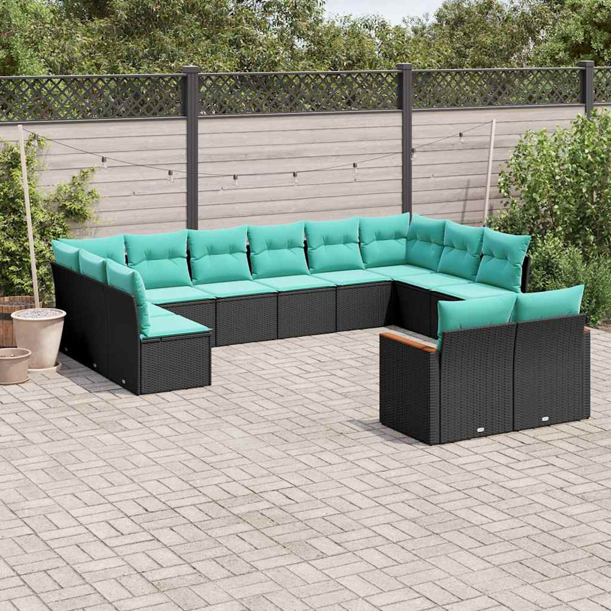 Ein modulares schwarzes Rattan-Sofa mit hellgrünen Kissen auf einer gepflasterten Terrasse.