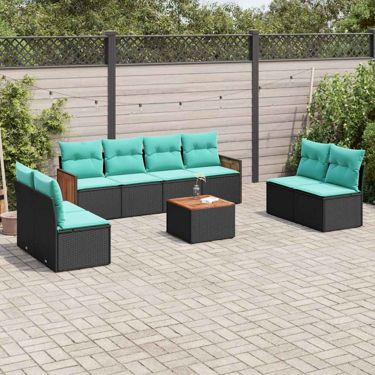 Conjunto de salón de exterior con módulos de ratán negro y cojines verde azulado sobre un patio pavimentado.