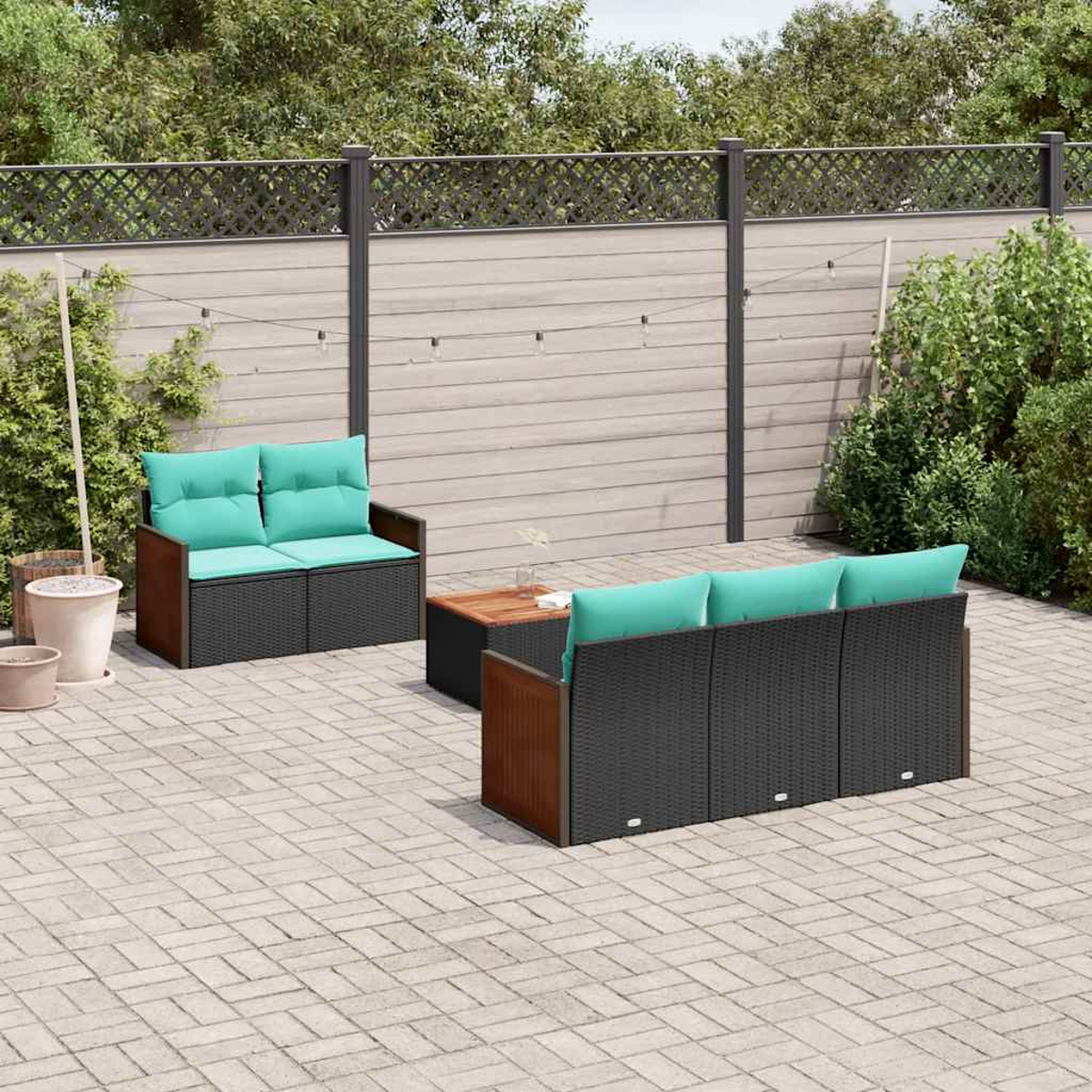 Gartenlounge-Set mit schwarzen Rattansofas, hellgrünen Kissen und Holztisch auf Steinpflaster.
