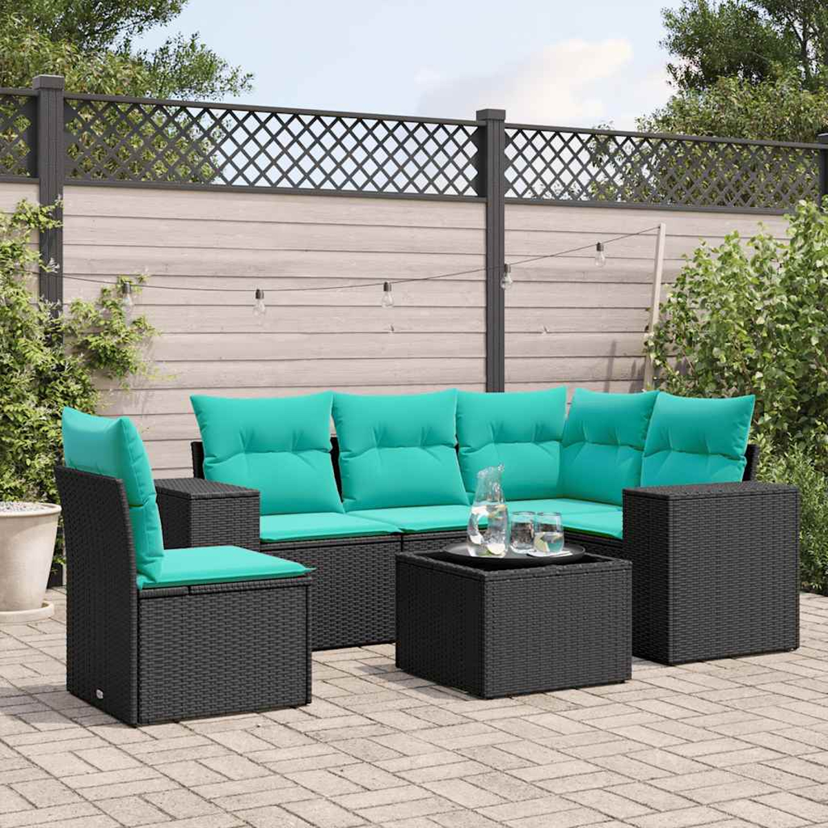 Gartenlounge mit schwarzen Rattansofas und türkisen Kissen, Couchtisch mit Glaskaraffe.